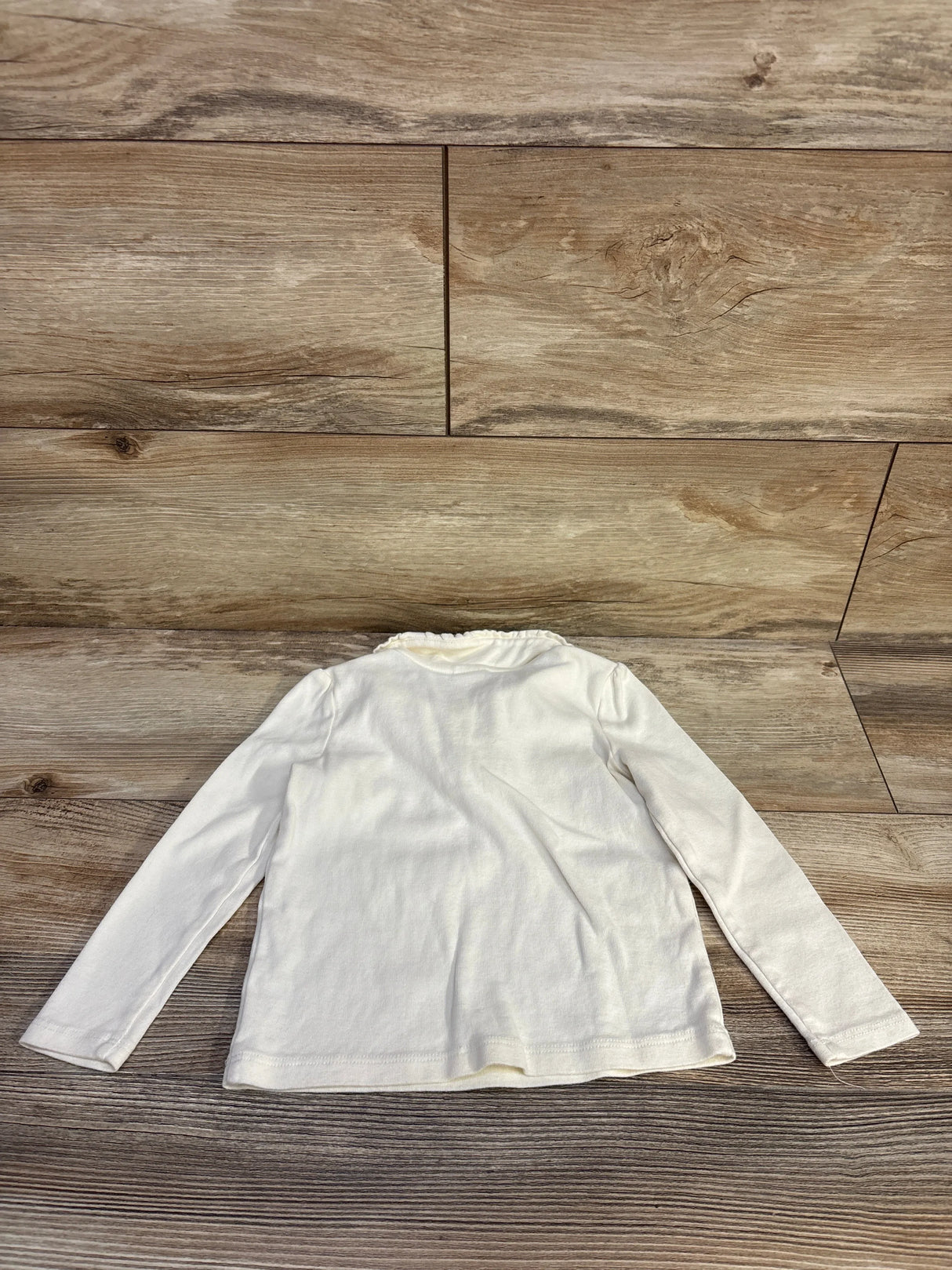 Back flat lay of Gymboree cream long sleeve toddler top showing ruffled Peter Pan collar on wood floor background