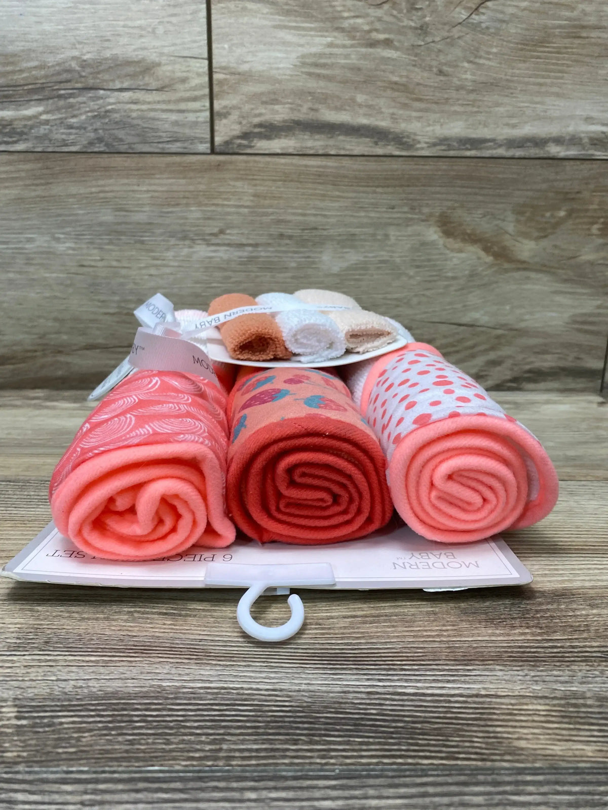 Front view of 6-piece peach hooded towel and washcloth set showing three rolled washcloths and patterned cloths on wood background