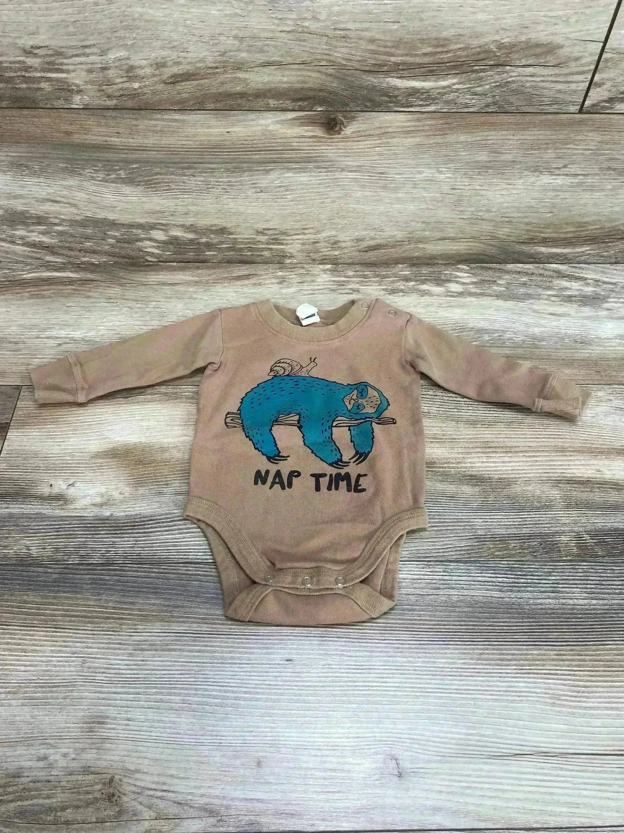 Flat lay of Little Pilgrim Nap Time sloth bodysuit 3-6M showing blue sloth graphic and crotch snaps on wood floor