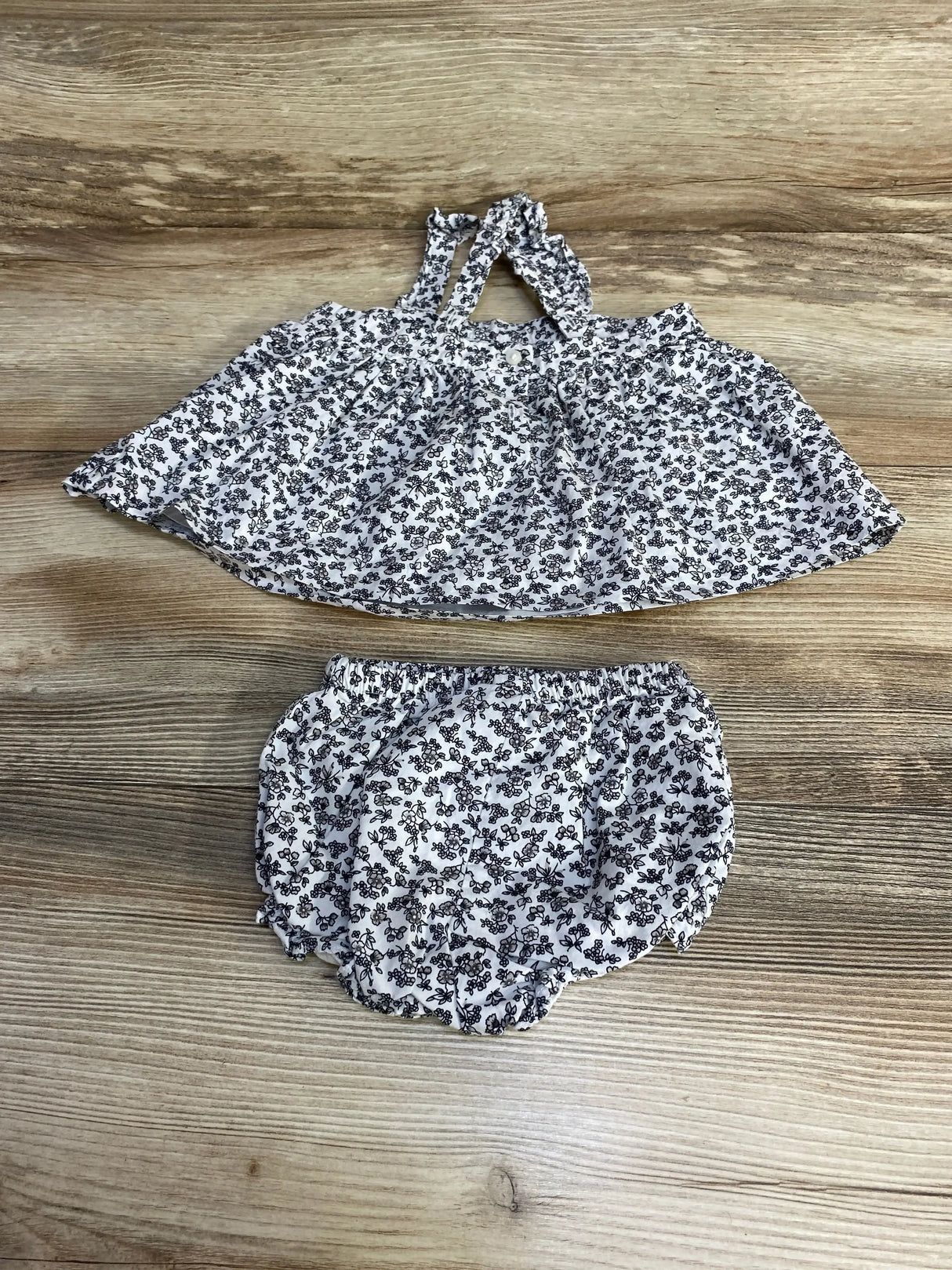 Flat-lay of Janie and Jack two-piece ditsy floral top and bloomers showcasing tie-shoulder straps and elastic waist on wood background