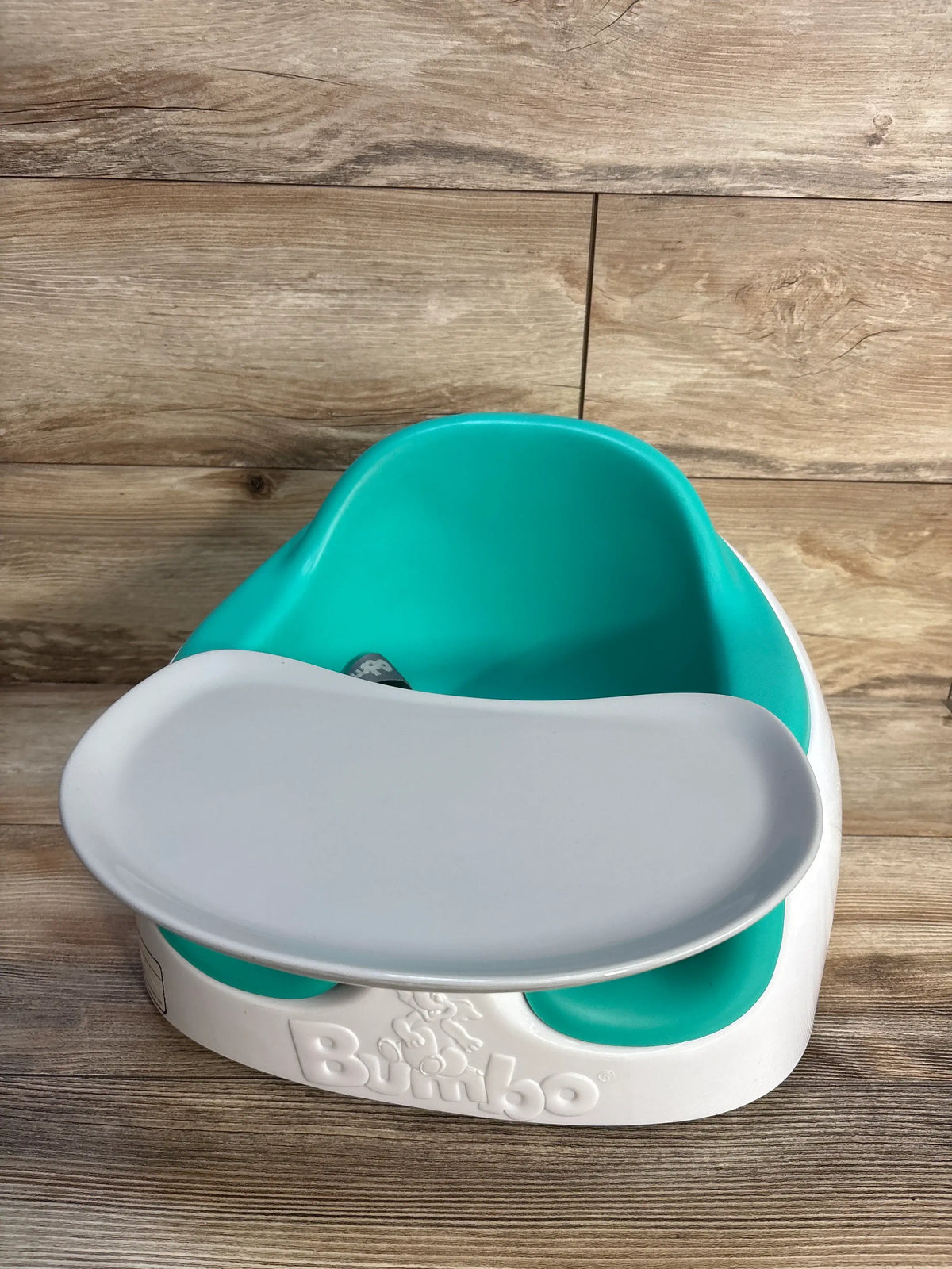 Front view of teal Bumbo Multi Seat showcasing its removable tray on a wood-look background