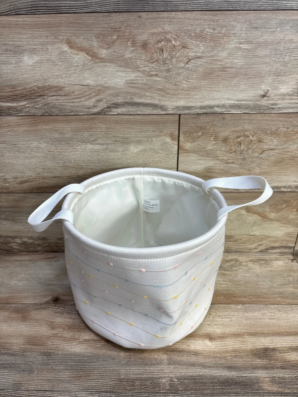 Angled top view of medium round bin showing slub stitching, interior lining, side handles, and pastel dot accents on wood
