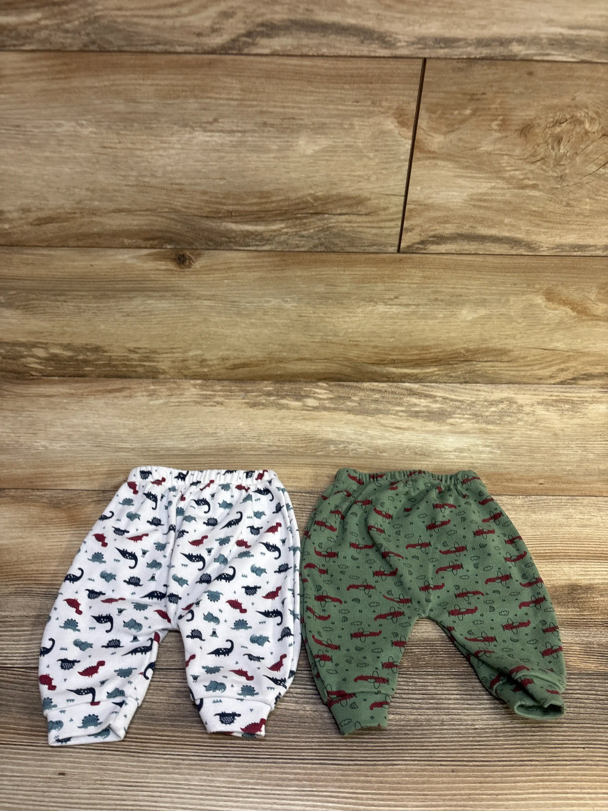 Top view of Hakochia 2pk pull-on pants in green and white with dinosaur prints on a wood floor