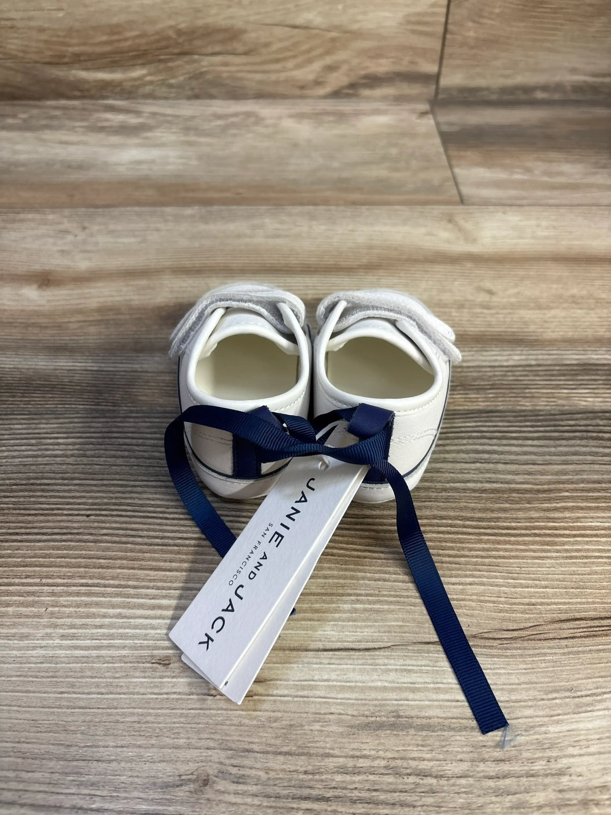 Top view of white Janie & Jack double strap sneakers showcasing the secure closures on a wood-look floor
