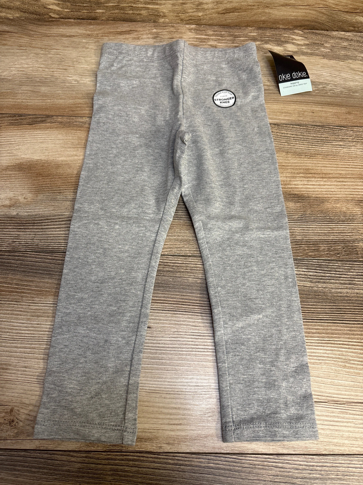 Gray okie dokie toddler leggings with tag on wood background, stronger knees patch visible