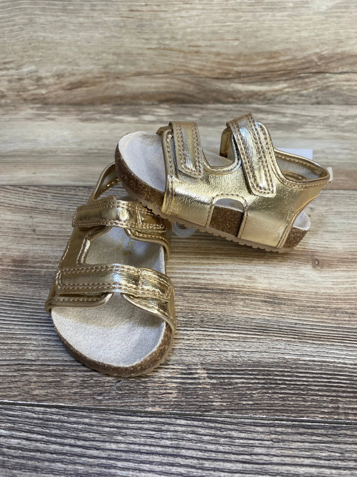 Gold toddler sandals with adjustable straps and cork soles on wood background