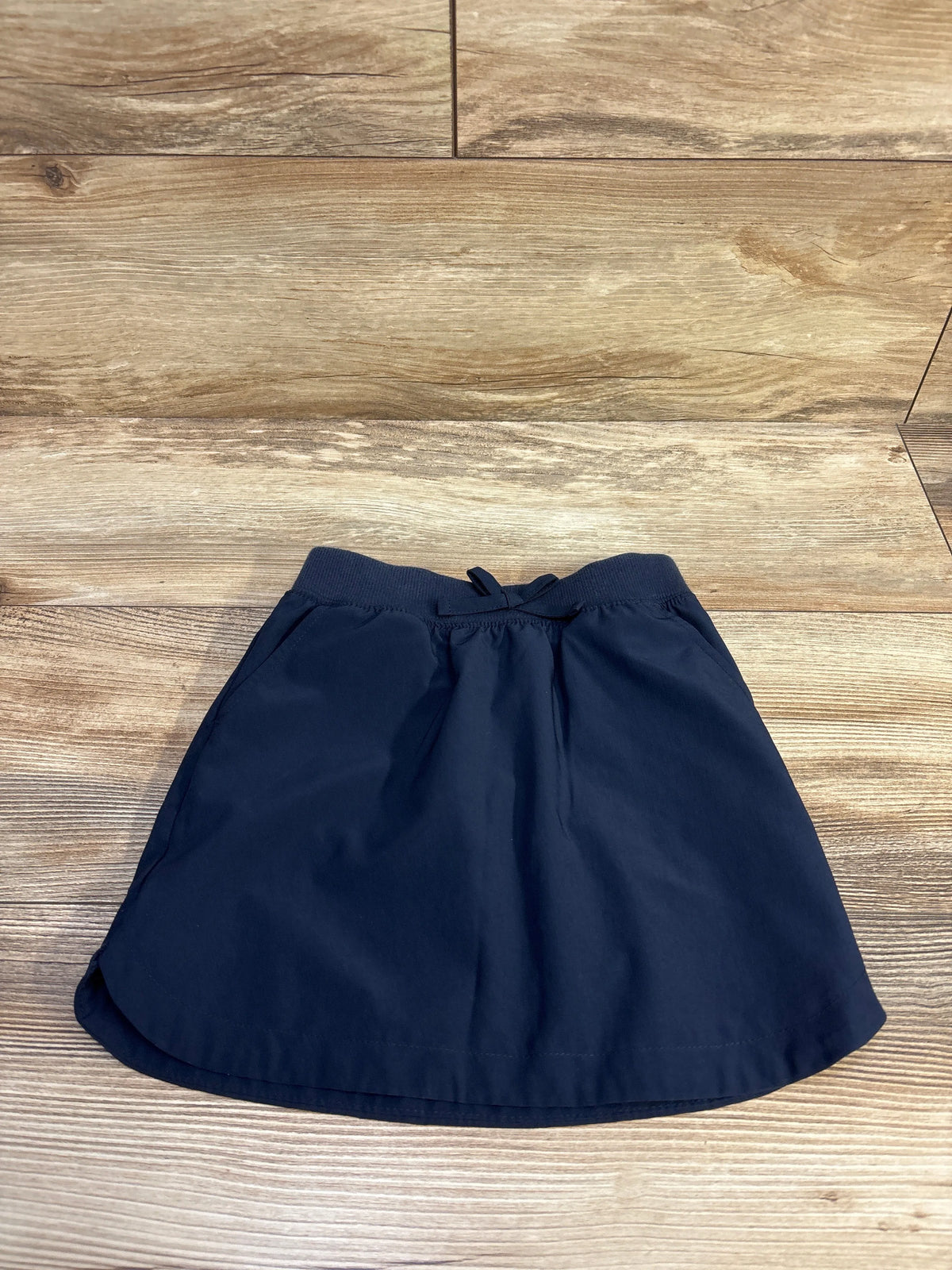 Top-down view of navy quick-dry skort (size 4T) showcasing ribbed elastic waistband with drawstring on a wood background