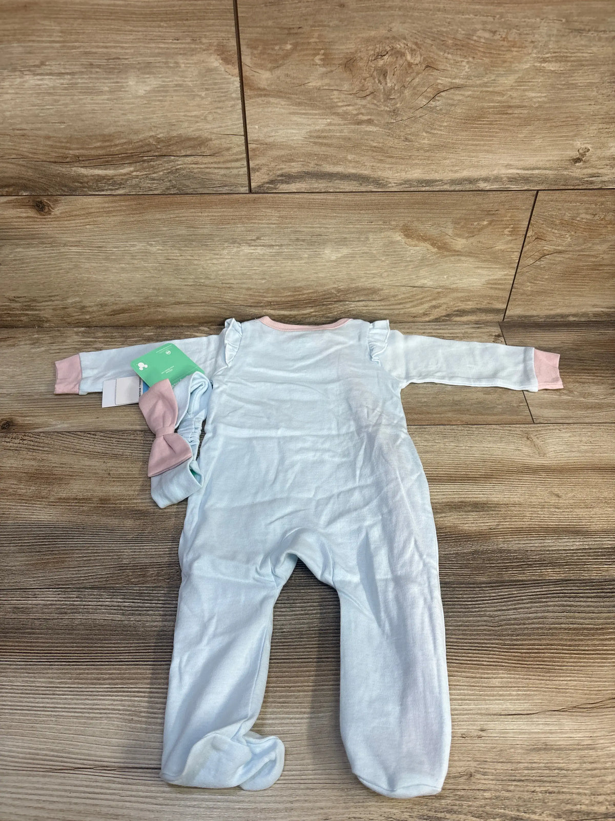 Front view of Disney Baby Dumbo sleeper and matching headband in blue with ruffled shoulders on a wood floor