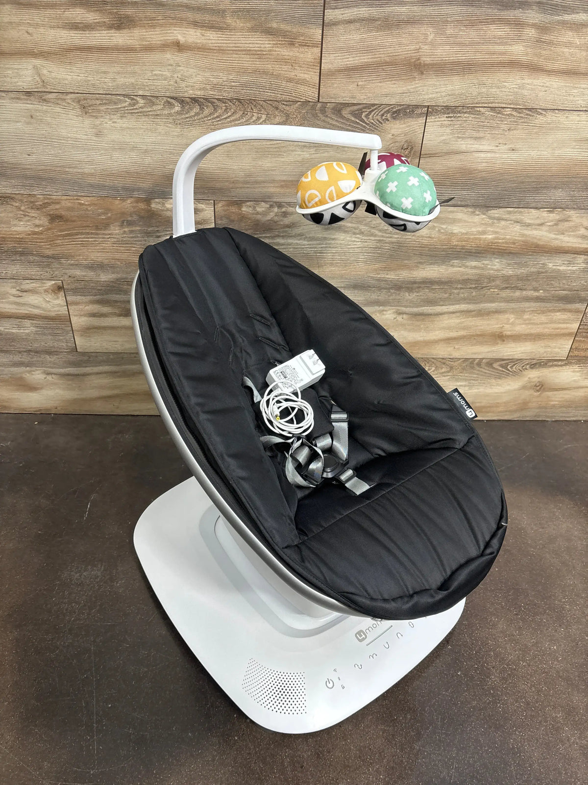 Angled view of 4moms mamaRoo Multi-Motion Baby Swing showing black seat, harness, toy mobile, and white base