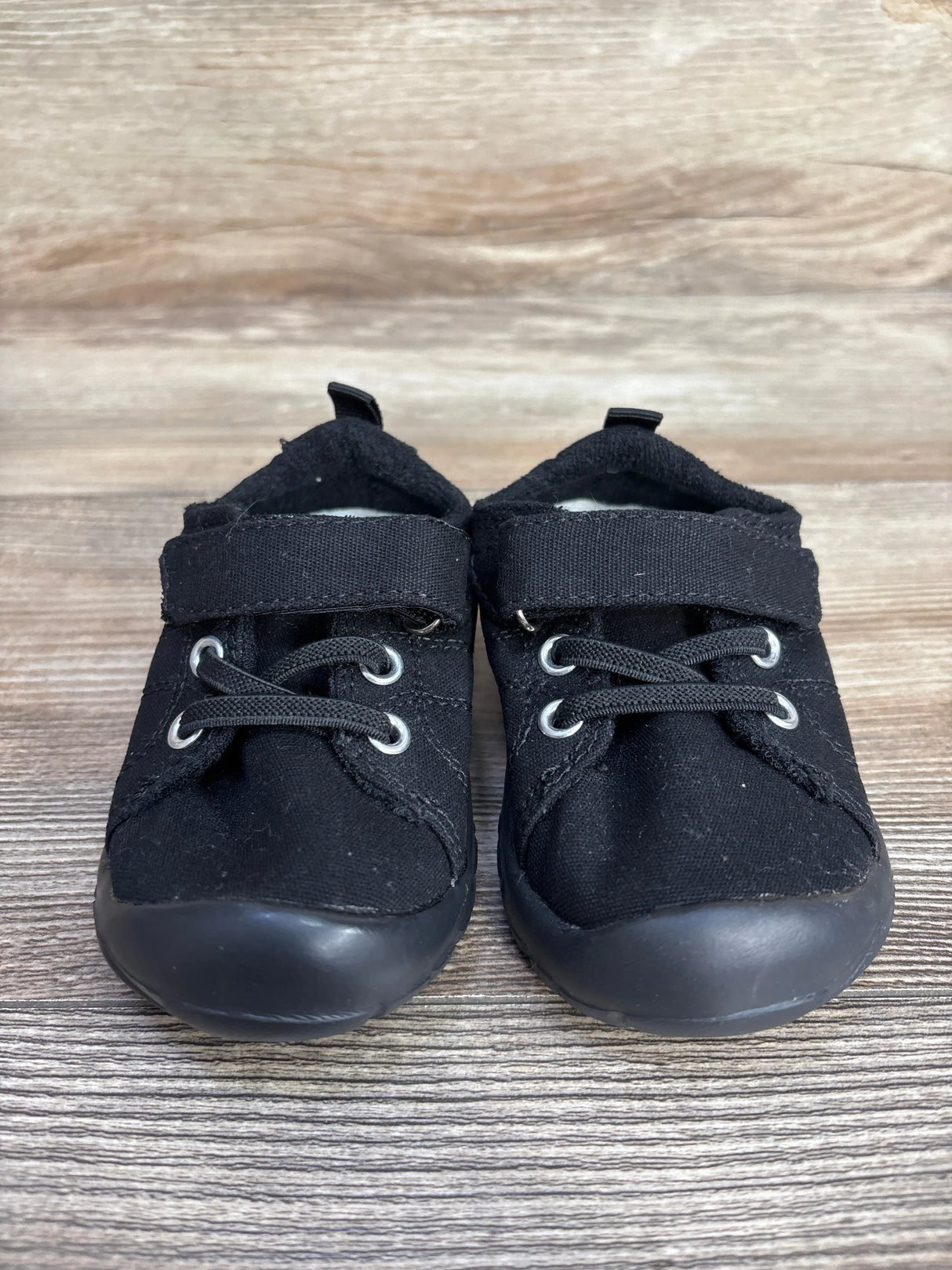 Pair of black toddler shoes with velcro straps and laces on wooden floor