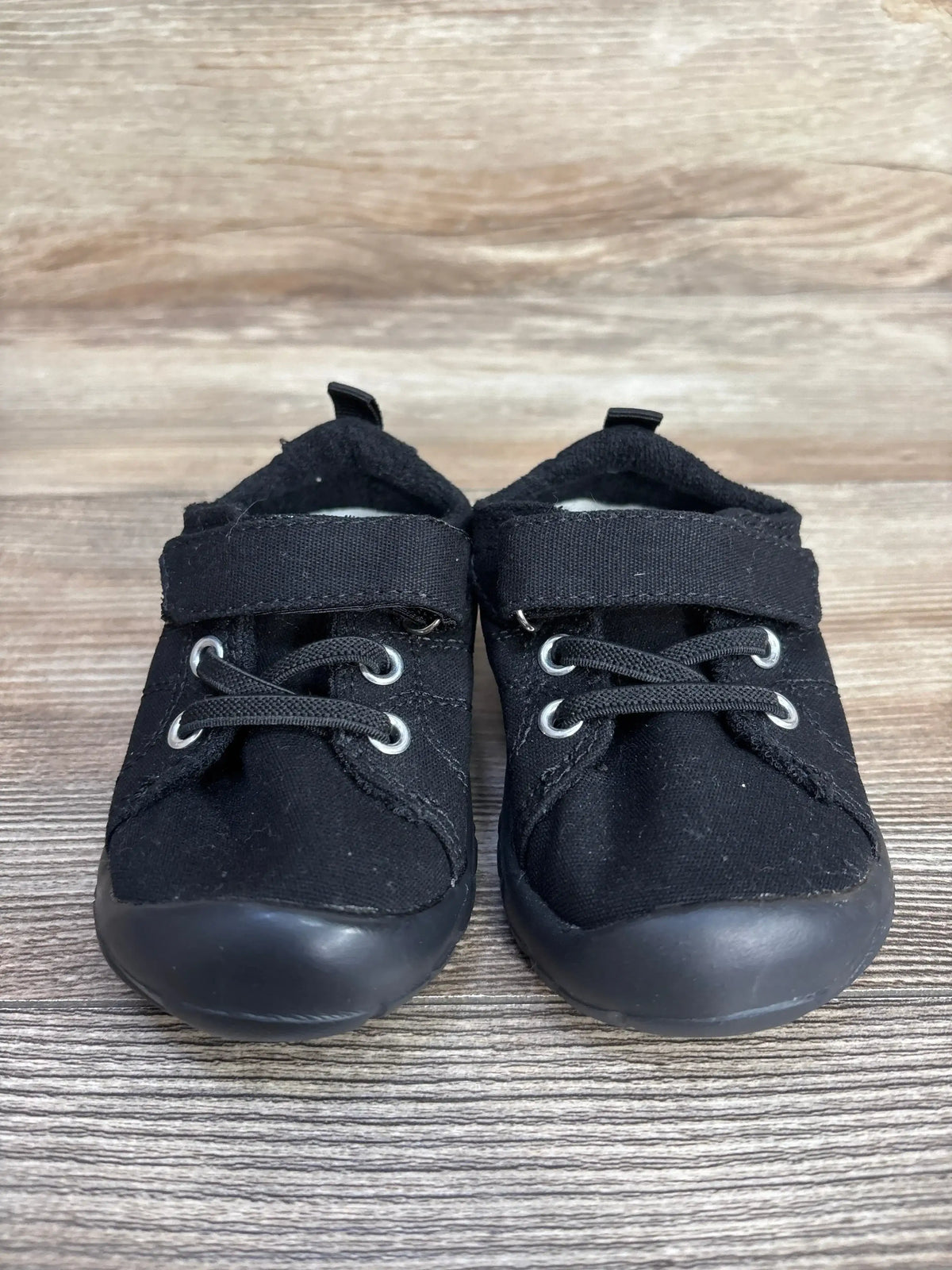 Pair of black toddler shoes with velcro straps and laces on wooden floor