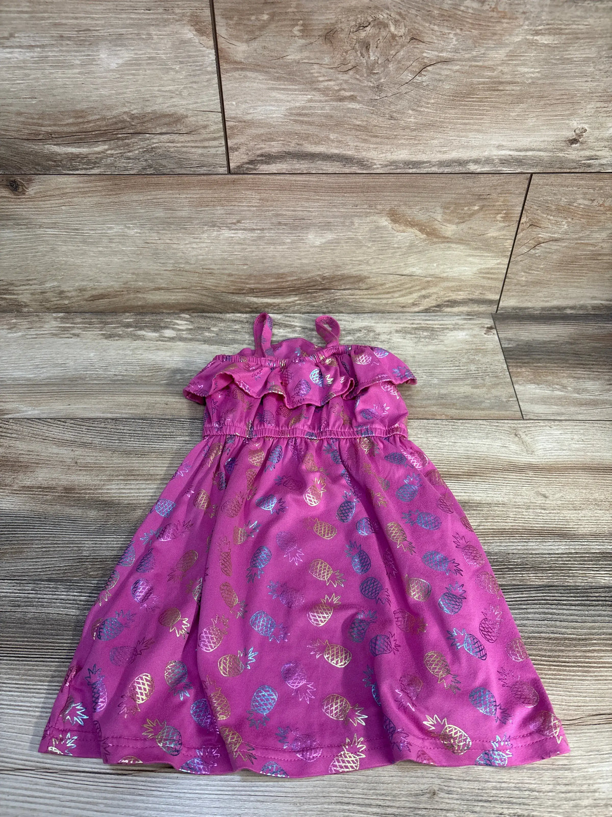 Front view of Picapino pineapple dress in purple size 24 months with ruffled straps and pineapple print on wood look background