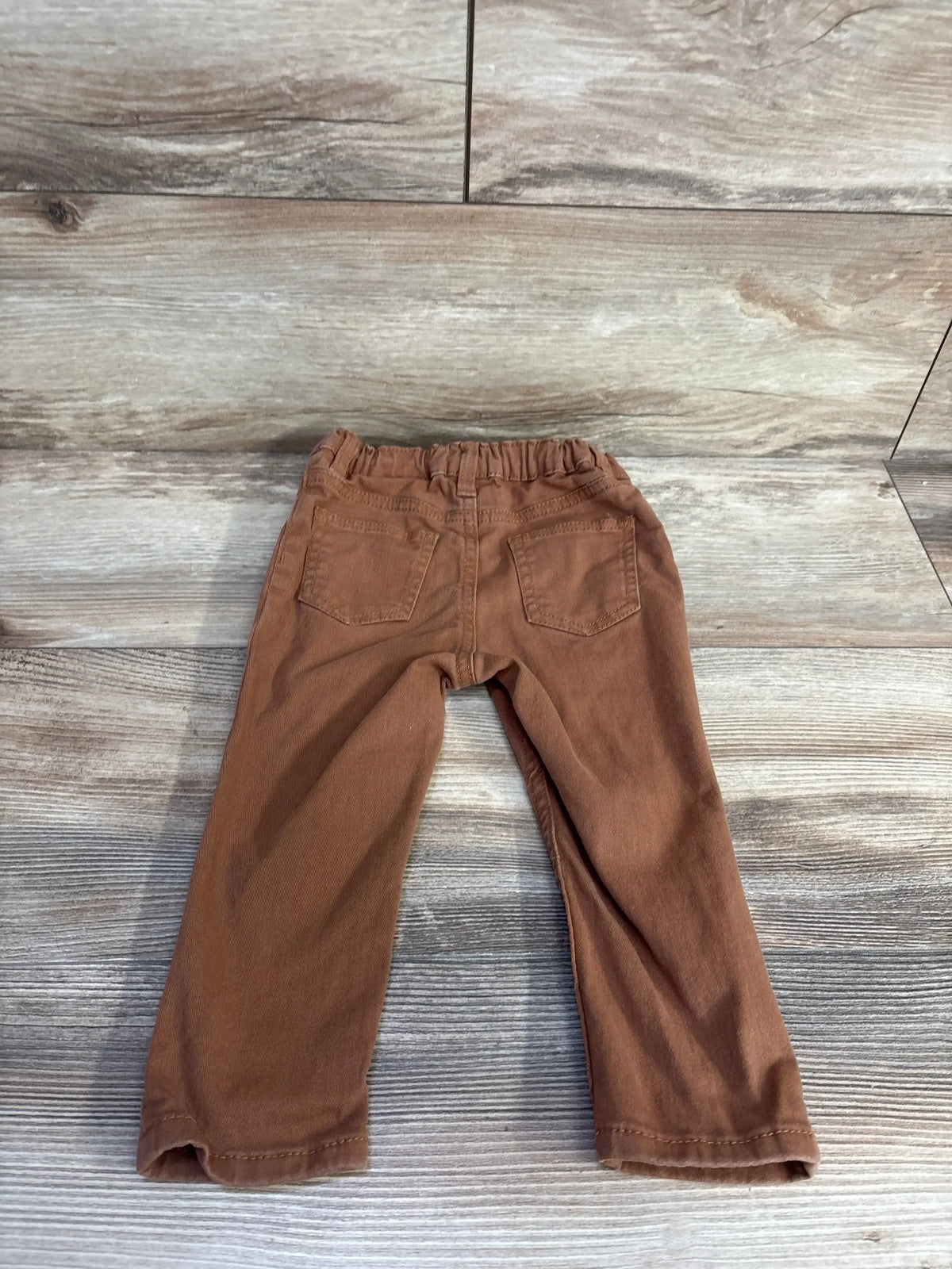 Back view of H and M twill trouser pants in brown showcasing elastic waistband and rear patch pockets on wood plank floor