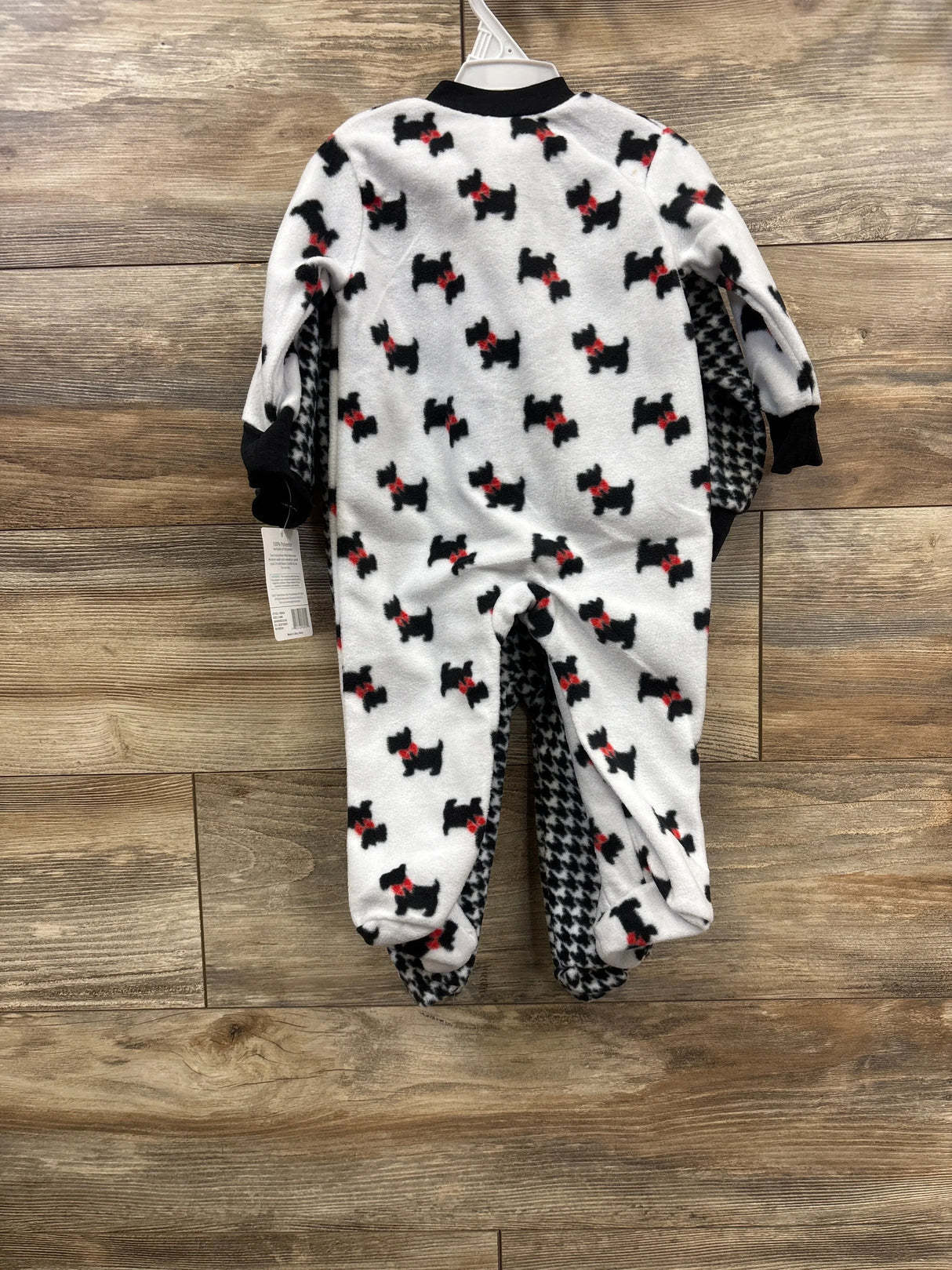White fleece baby sleeper with black dog and red bow pattern, displayed on wood background
