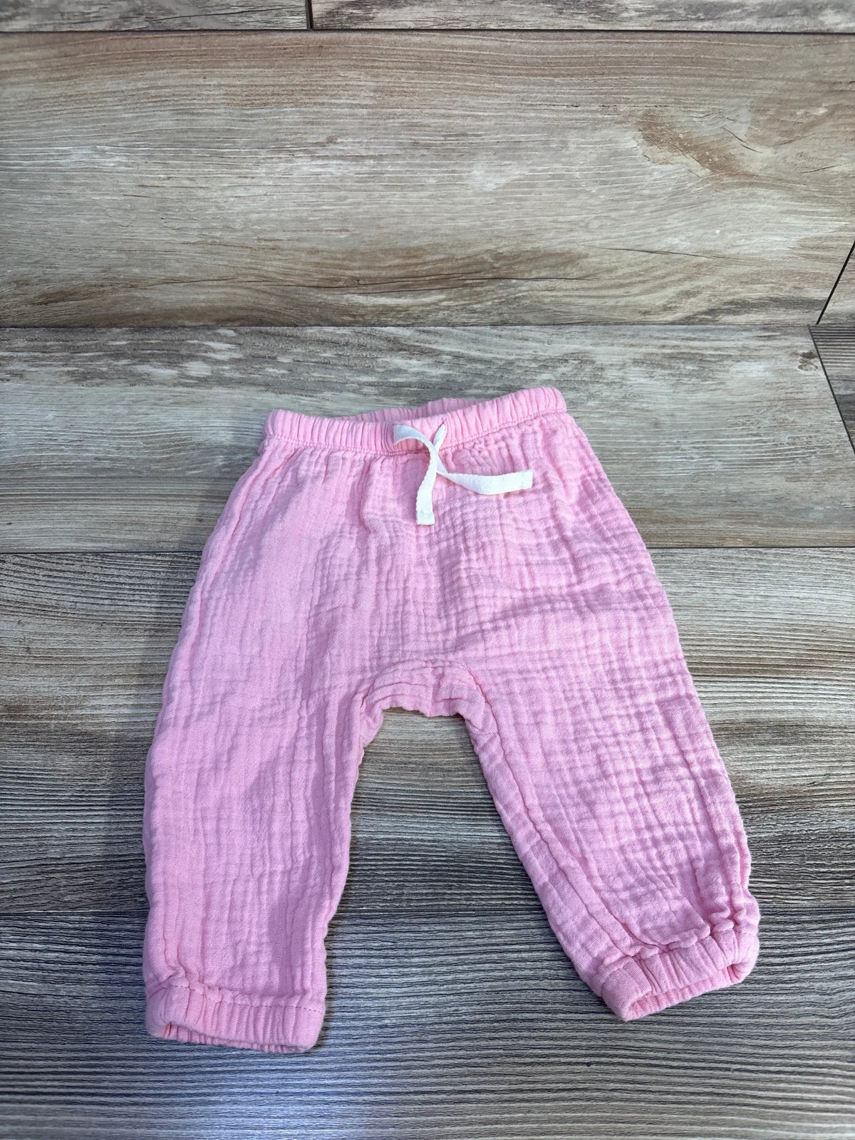 Front view of pink Old Navy gauze pull-on pants in size 3 to 6 months with drawstring on wood-look background