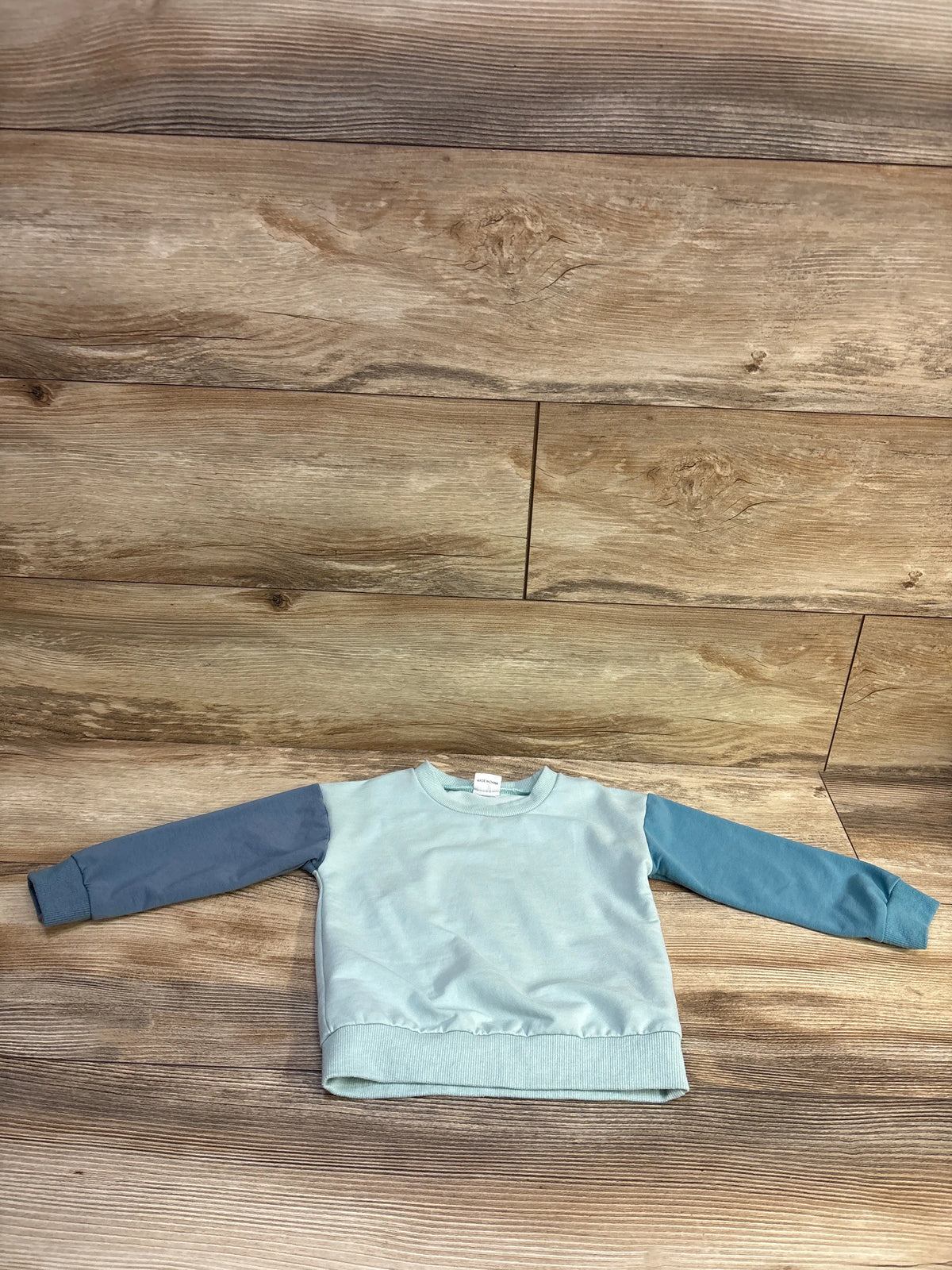 Top view of a blue Shein pullover sweatshirt in size 18 to 24 months with long sleeves and ribbed cuffs and hem on wood