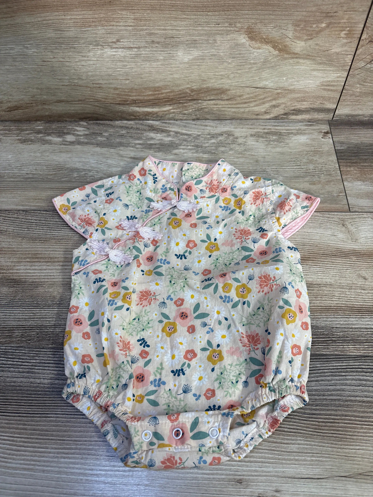 Flat lay of cream kimono-style floral baby romper showing front knot ties and snap crotch on wood background