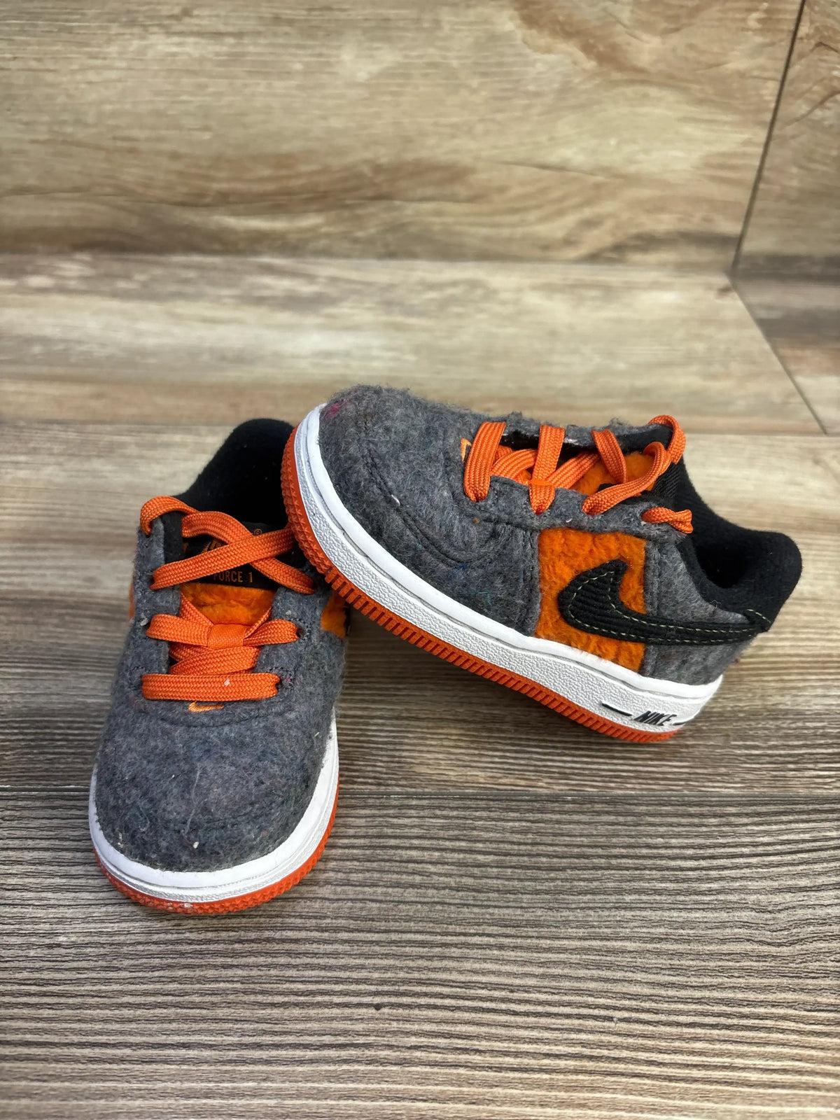 Front and side of toddler Nike Force 1 sneakers with gray felt upper, orange laces, black Swoosh, size 5C on wood background