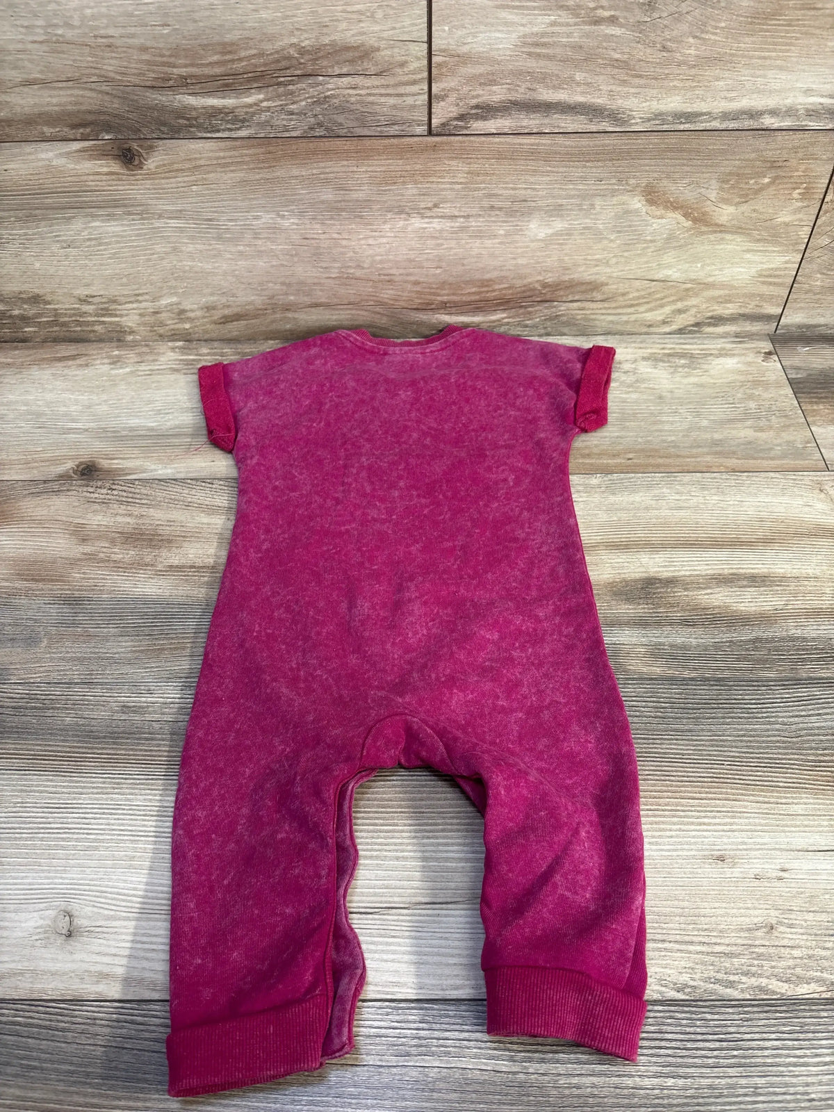 Back view of Disney Baby Minnie Mouse magenta 12m jumpsuit with short sleeves, cuffed legs, washed fabric on wood floor