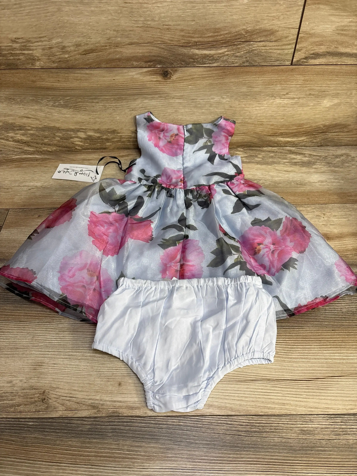 Front view of 2-piece toddler floral dress with pink rose print and matching white bloomers on wood floor