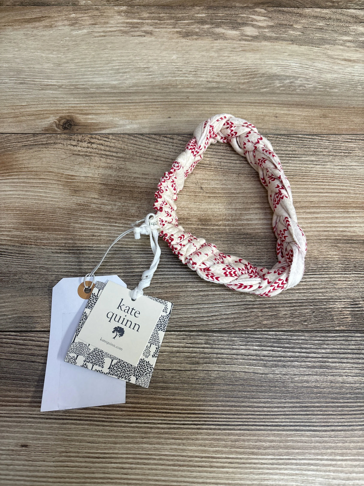 Kate Quinn kids braided white and red patterned headband with tag on wooden surface