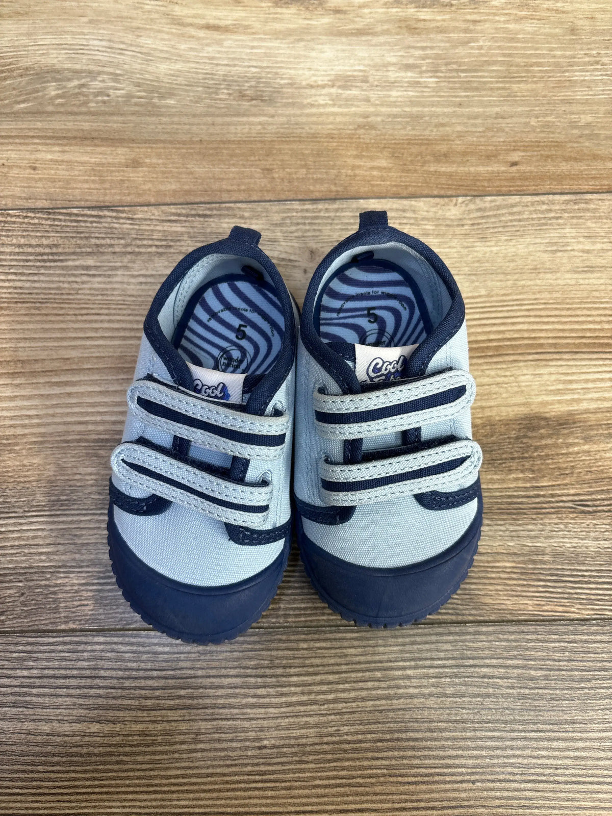 Front view of blue Magical Internet Money Two Strap Bump Tow Sneakers with two straps and navy toe caps on wood grain