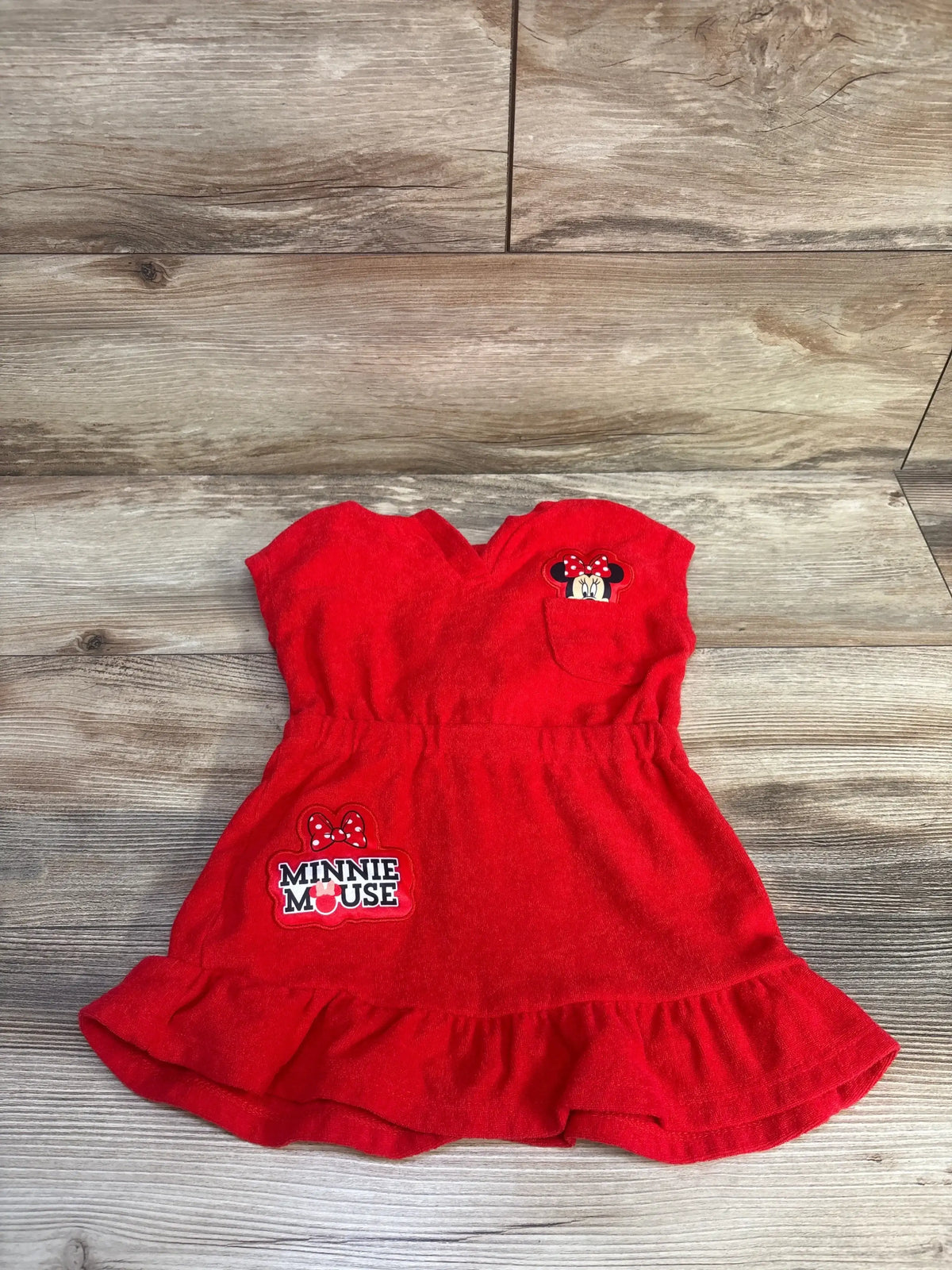 Flat lay of red Minnie Mouse terry swim cover-up 2T with chest and logo patches, elastic waist and ruffled hem on wood floor