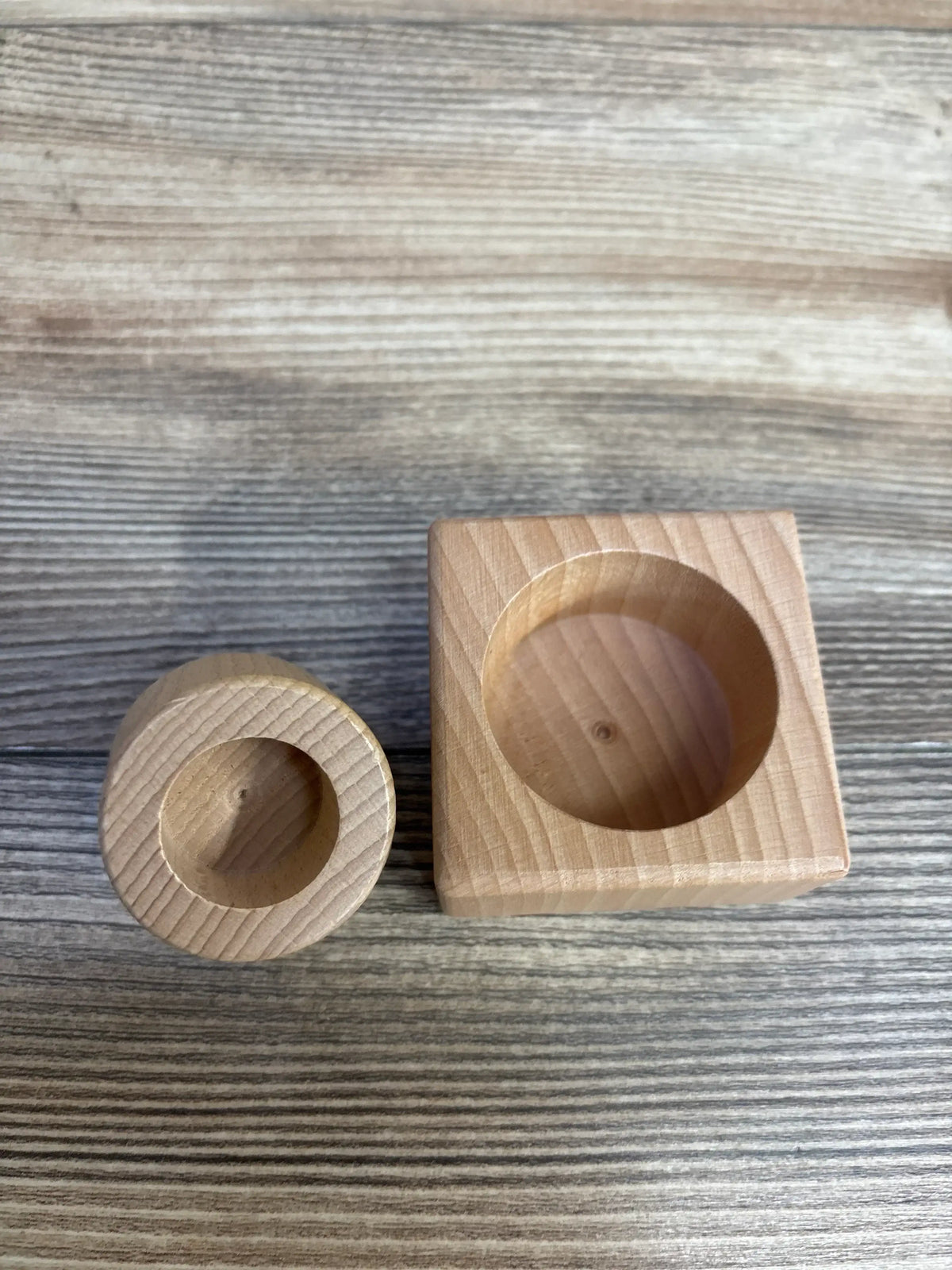 Top view of Lovevery Pincer Puzzle wooden base pieces showing round and square blocks with circular cutouts on wood plank floor