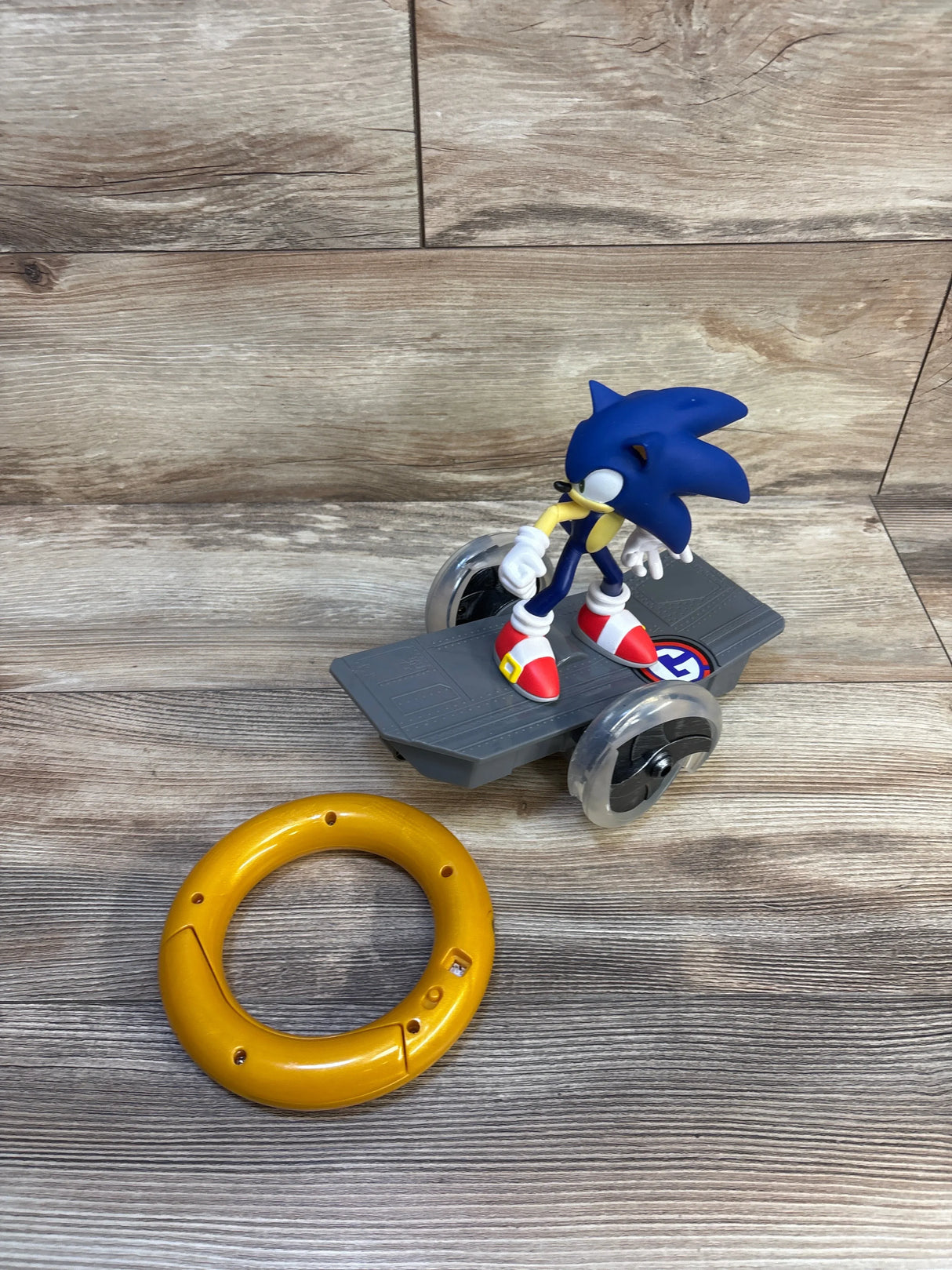 Sonic the Hedgehog toy figure on wheeled skateboard with large yellow toy ring, wood background