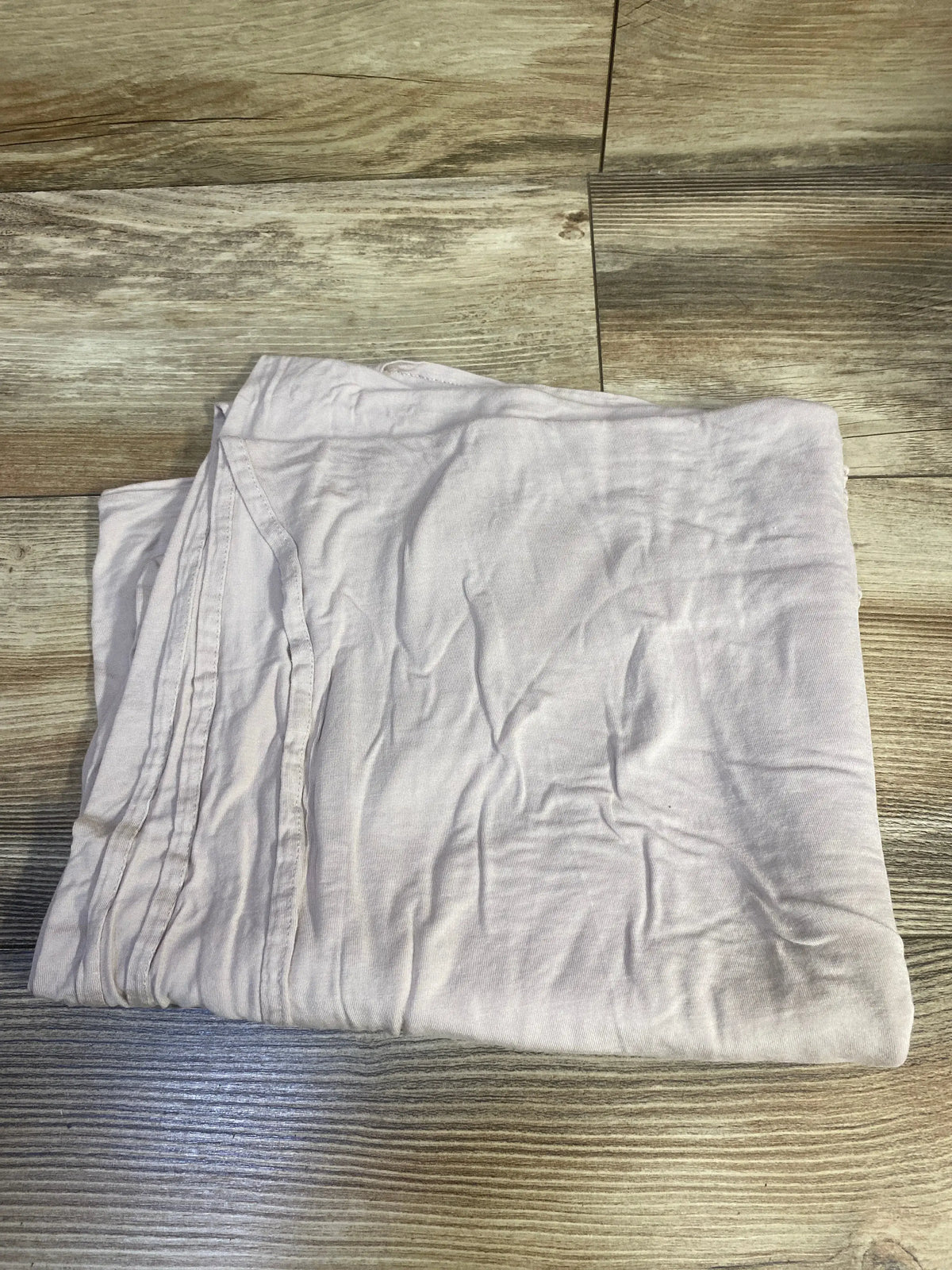 Folded Little Unicorn stretch knit viscose swaddle blanket with stitched edging on a wood floor