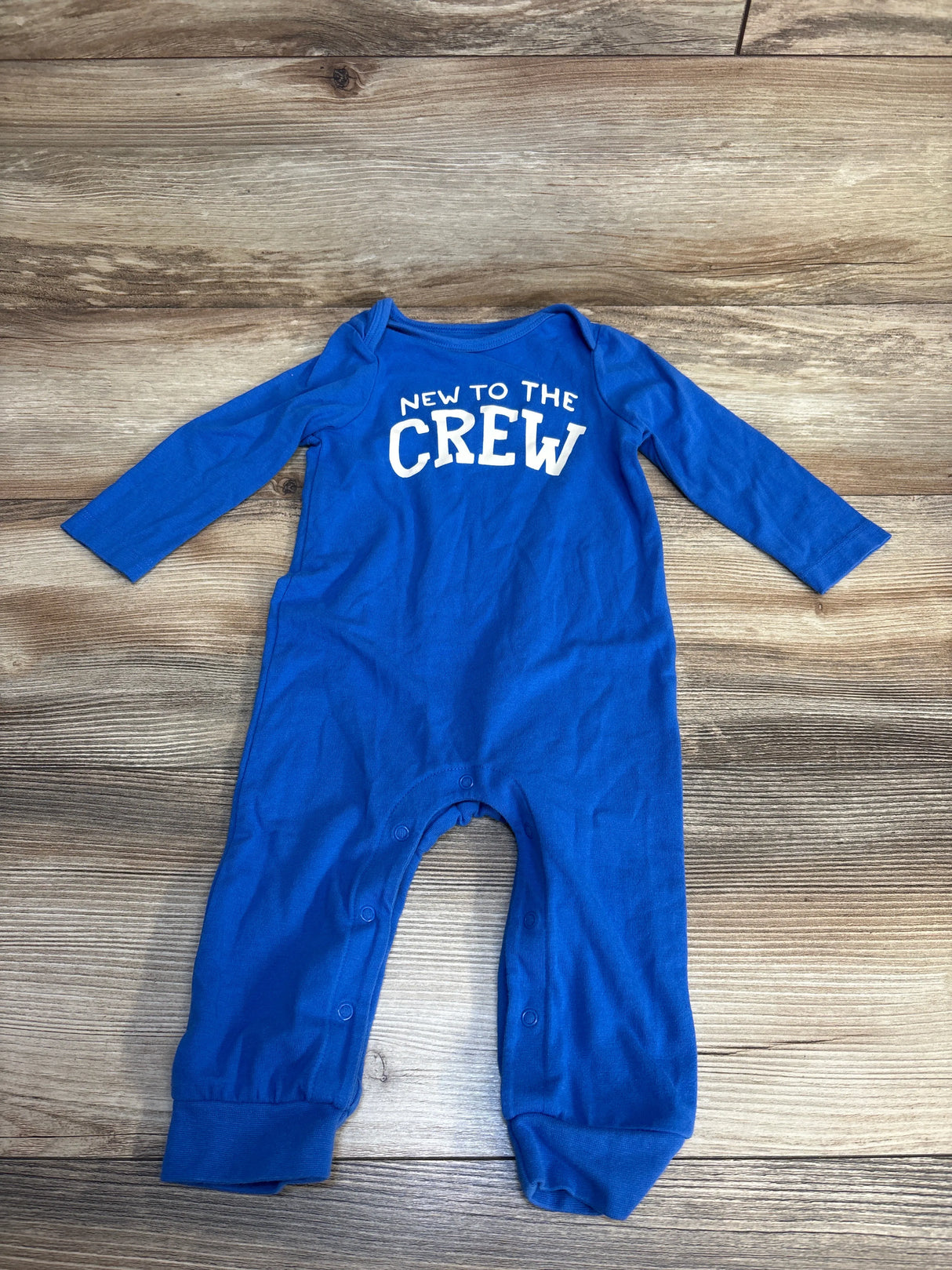Blue baby onesie with 'New to the Crew' print, long sleeve newborn outfit on wood floor