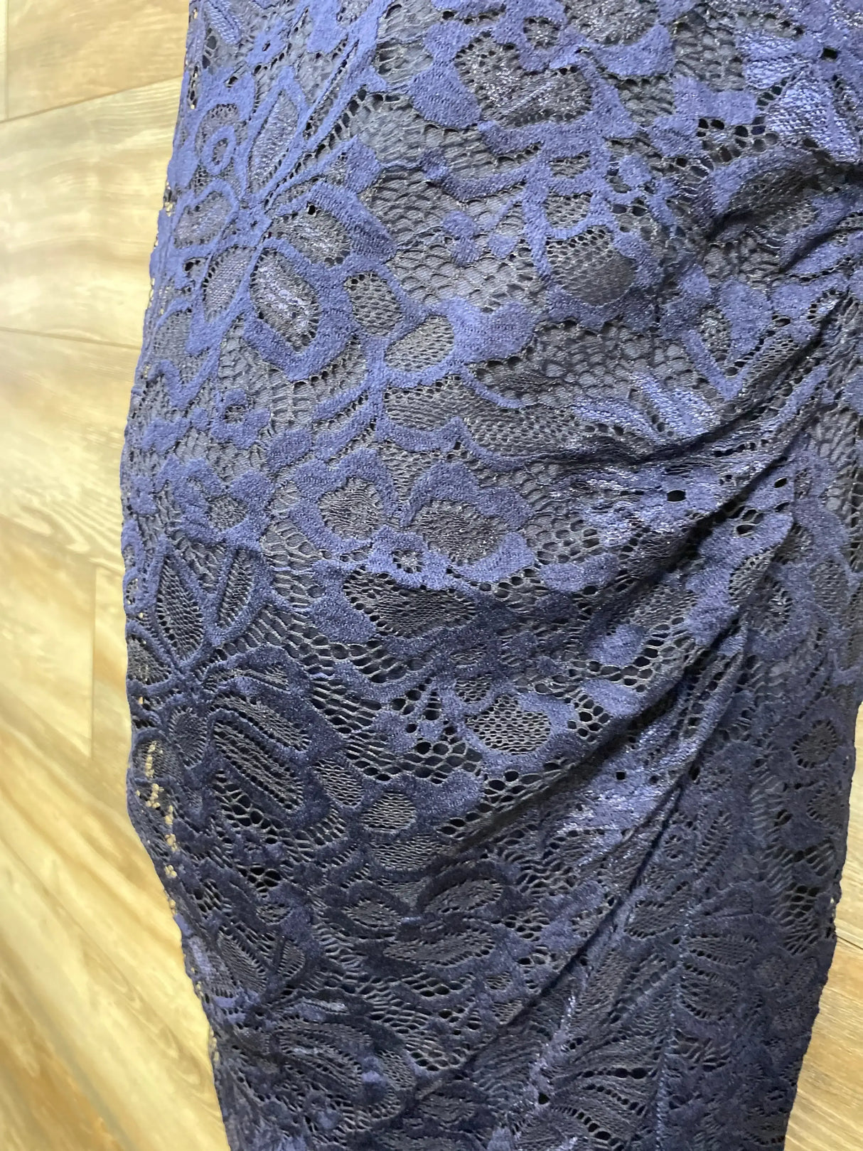 Close-up side view of Pink Blush navy maternity lace dress showing floral lace overlay and ruching on light wood background