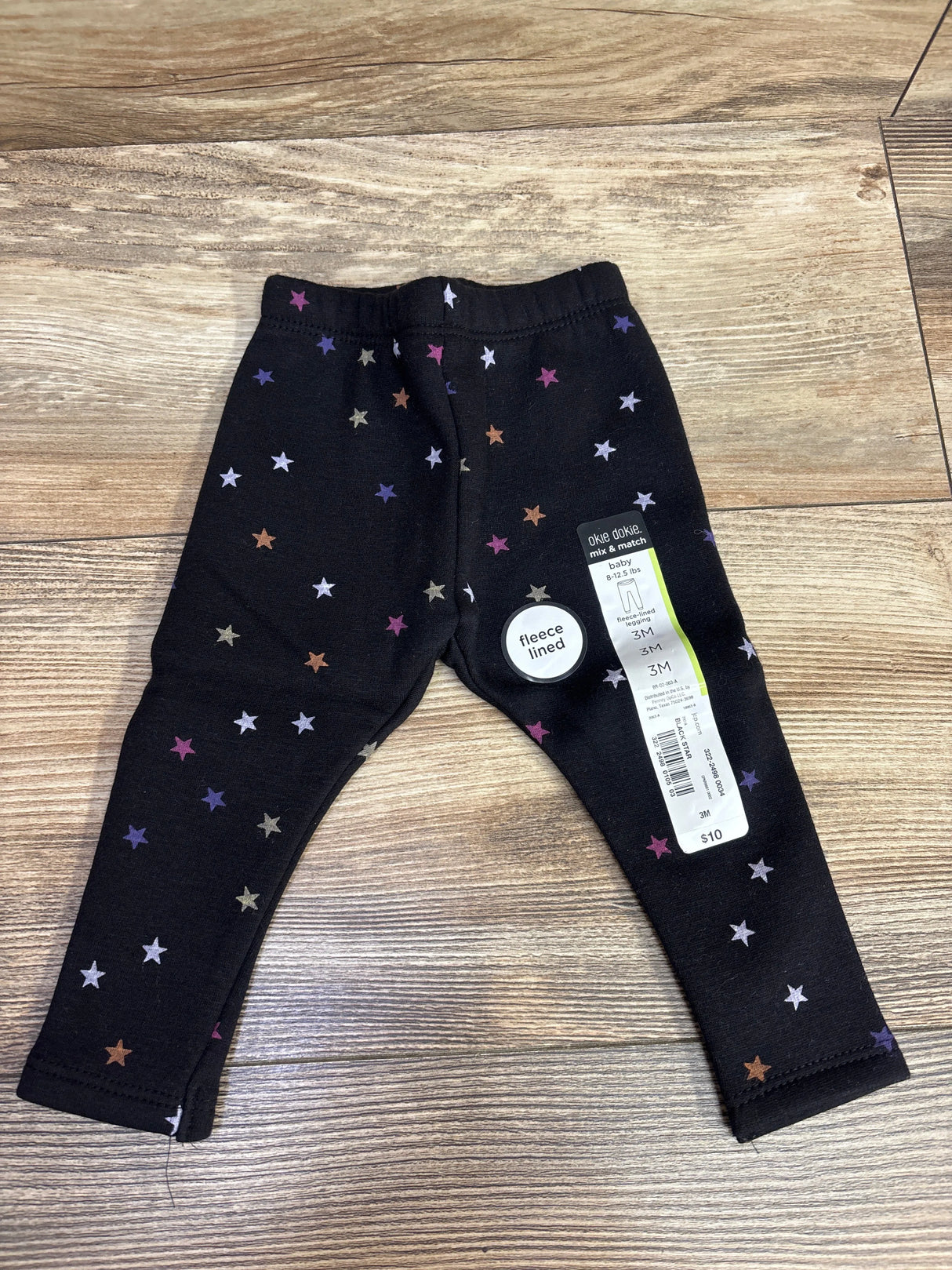 Black baby fleece-lined leggings with multicolor star pattern, size 3M, $10 price tag on wooden floor
