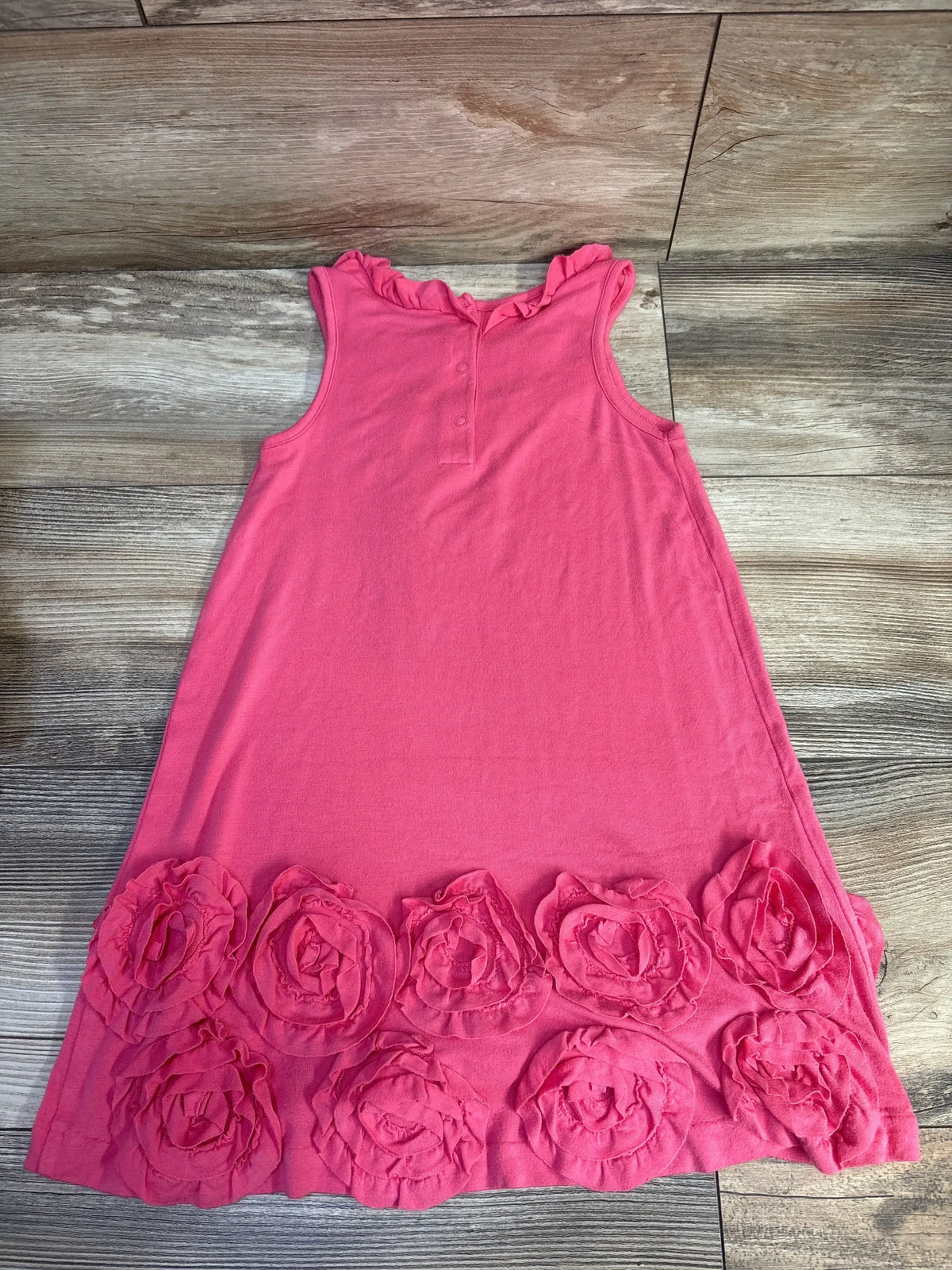 Flat-lay front of hot pink Janie & Jack rosette knit dress showcasing layered fabric roses along the hem on a wood floor