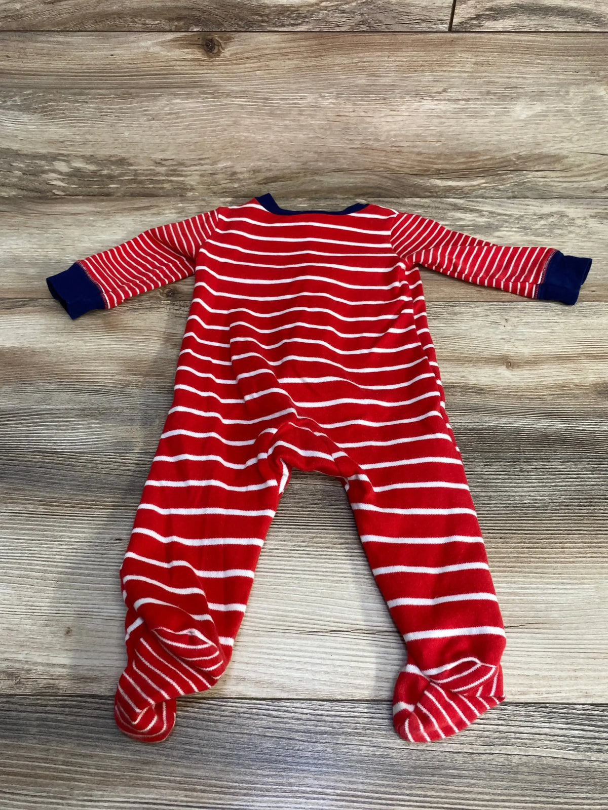 Flat lay of Carter’s red and white striped footed sleeper showcasing navy cuffs and closed feet on a wood floor background