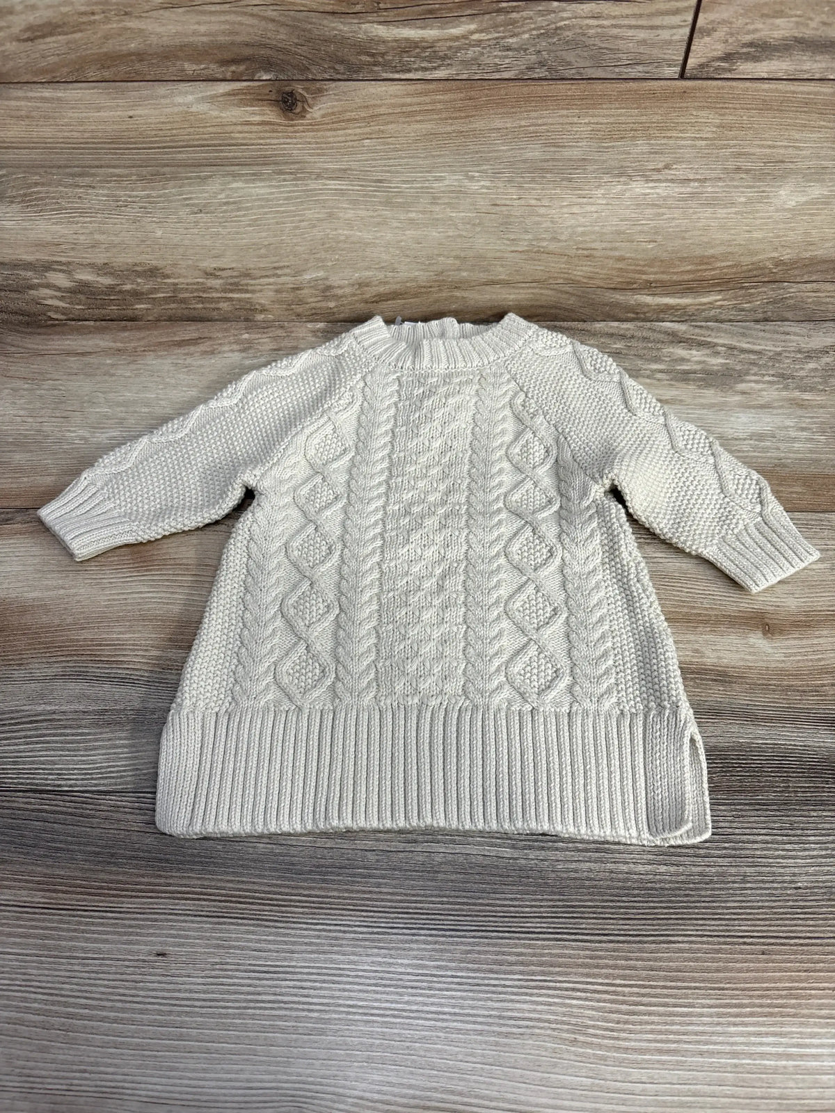 Flat lay of beige Baby Gap cable knit sweater dress showing cable and seed stitch pattern, ribbed hem on wood background