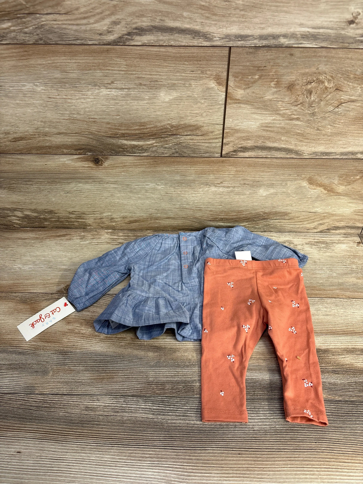 Baby girl outfit with blue long-sleeve top and orange floral leggings on wood floor
