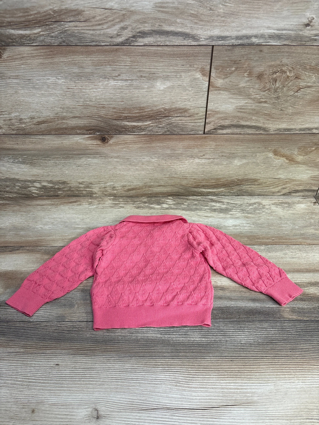 Back view of Janie and Jack pink crochet sweater showcasing diamond cable knit pattern with wood plank floor background