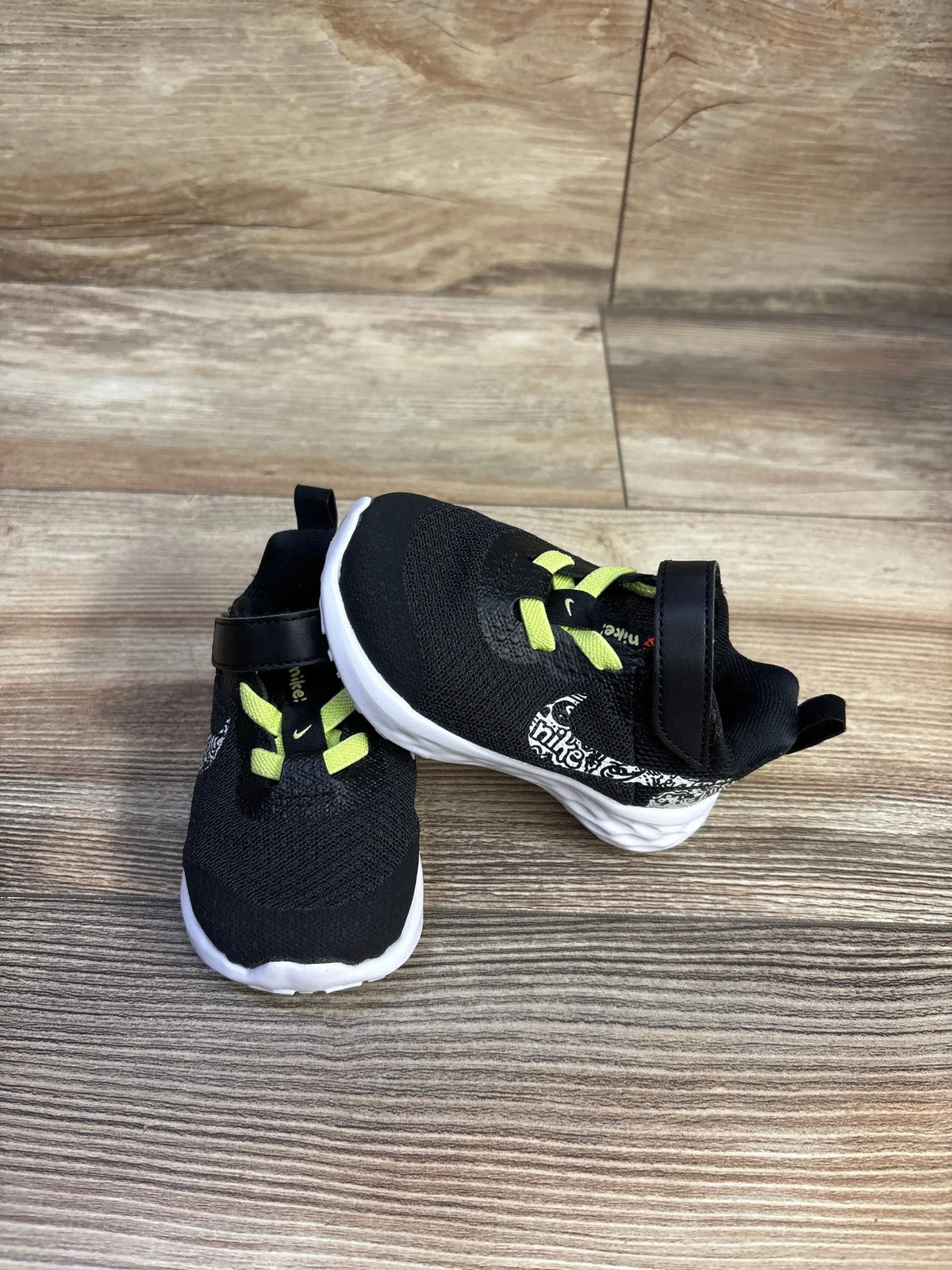 Angled view of Nike toddler sneakers with black knit, neon yellow elastic laces, Velcro strap, and white sole