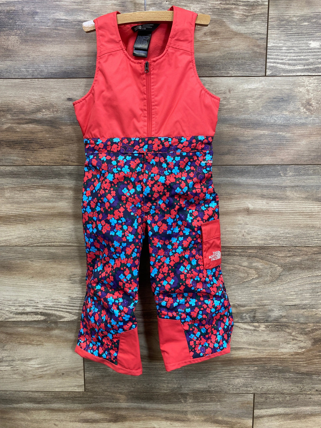 Red and floral North Face kids' snow bib with blue and red flowers on wood background