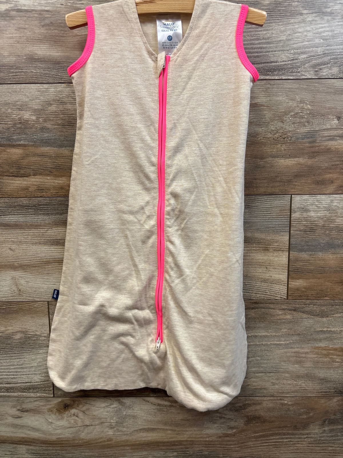 Front view of Halo SleepSack Ideal Temp Swaddle in oatmeal, size 0-6 months showcasing pink zipper and trim on wood floor