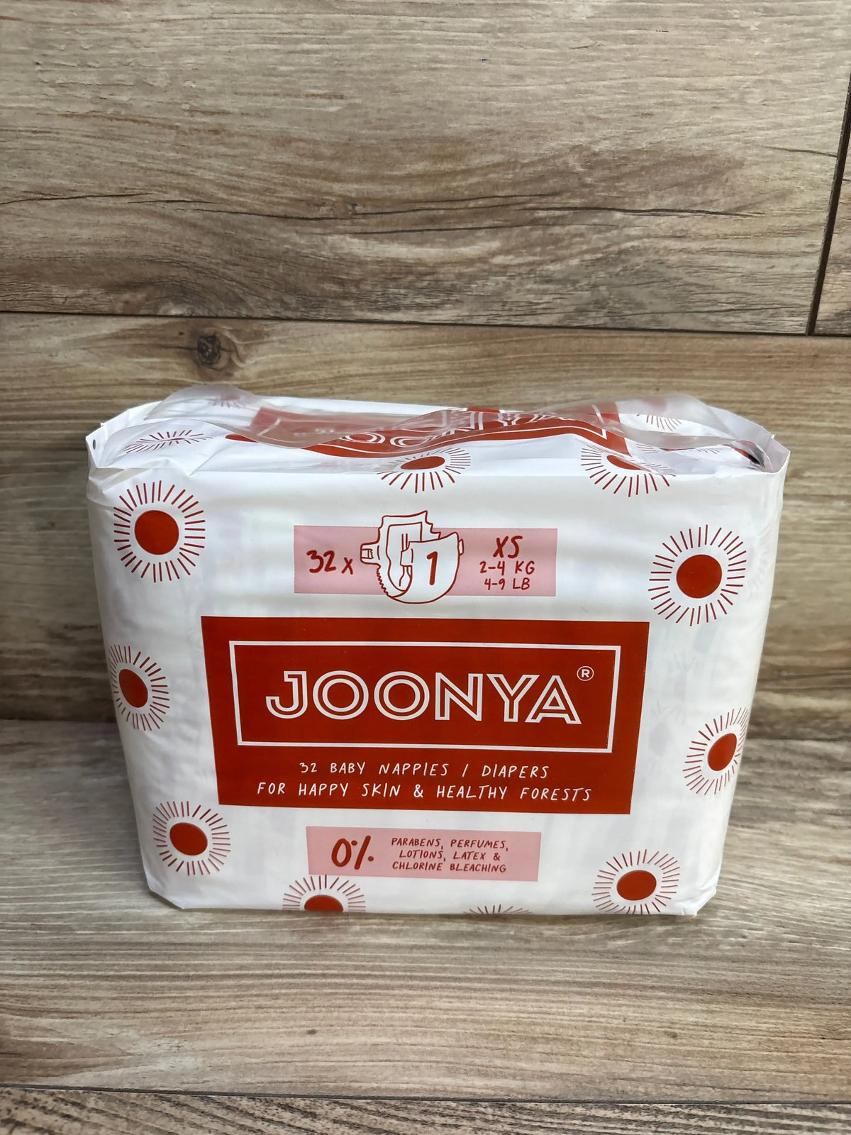 Front view of JOONYA Size 1 (Newborn) 32-count diaper pack showing brand logo and 0 percent parabens claim on wood background