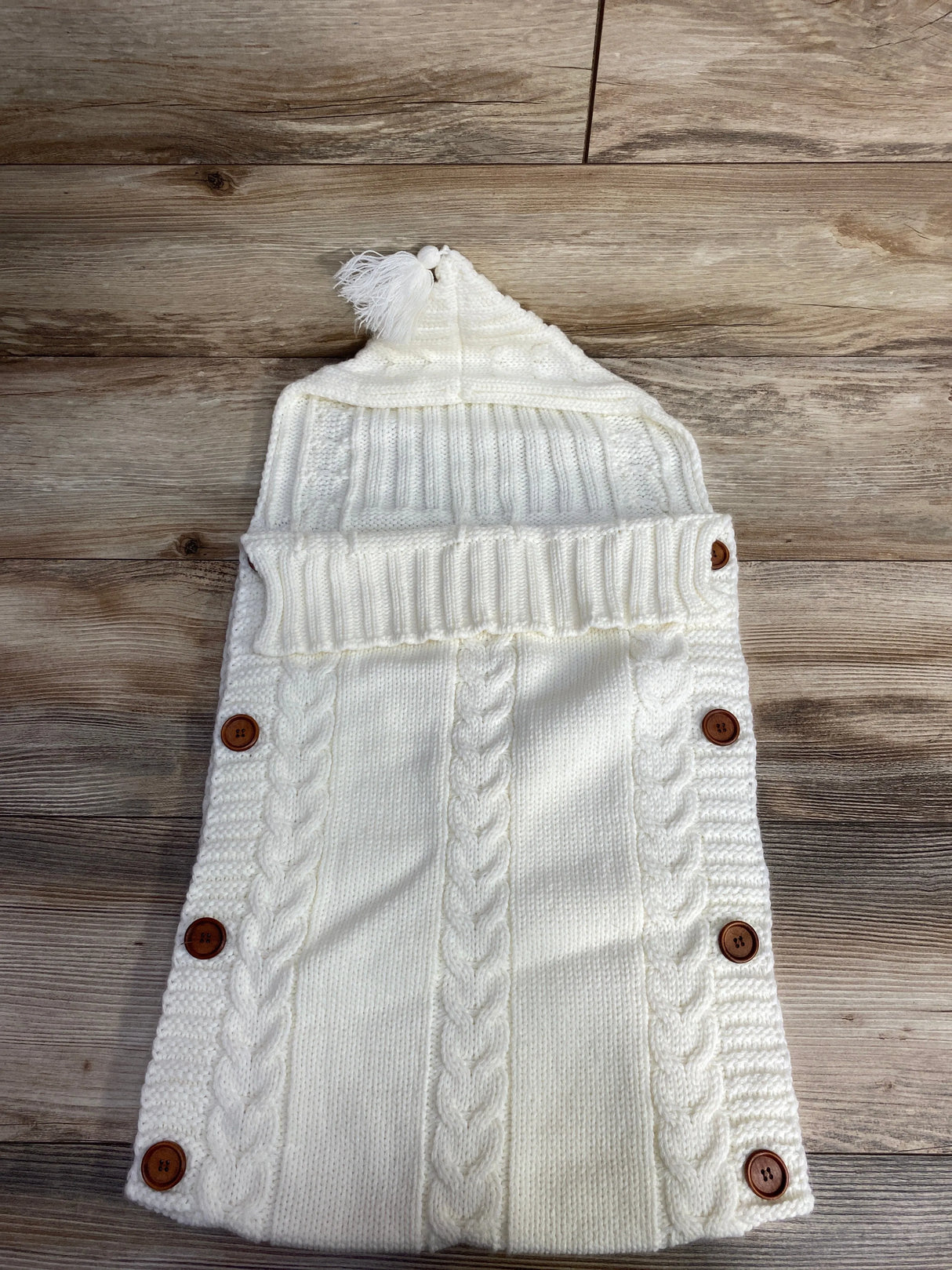 White knit baby sleeping bag with wooden buttons and hood, on wooden floor