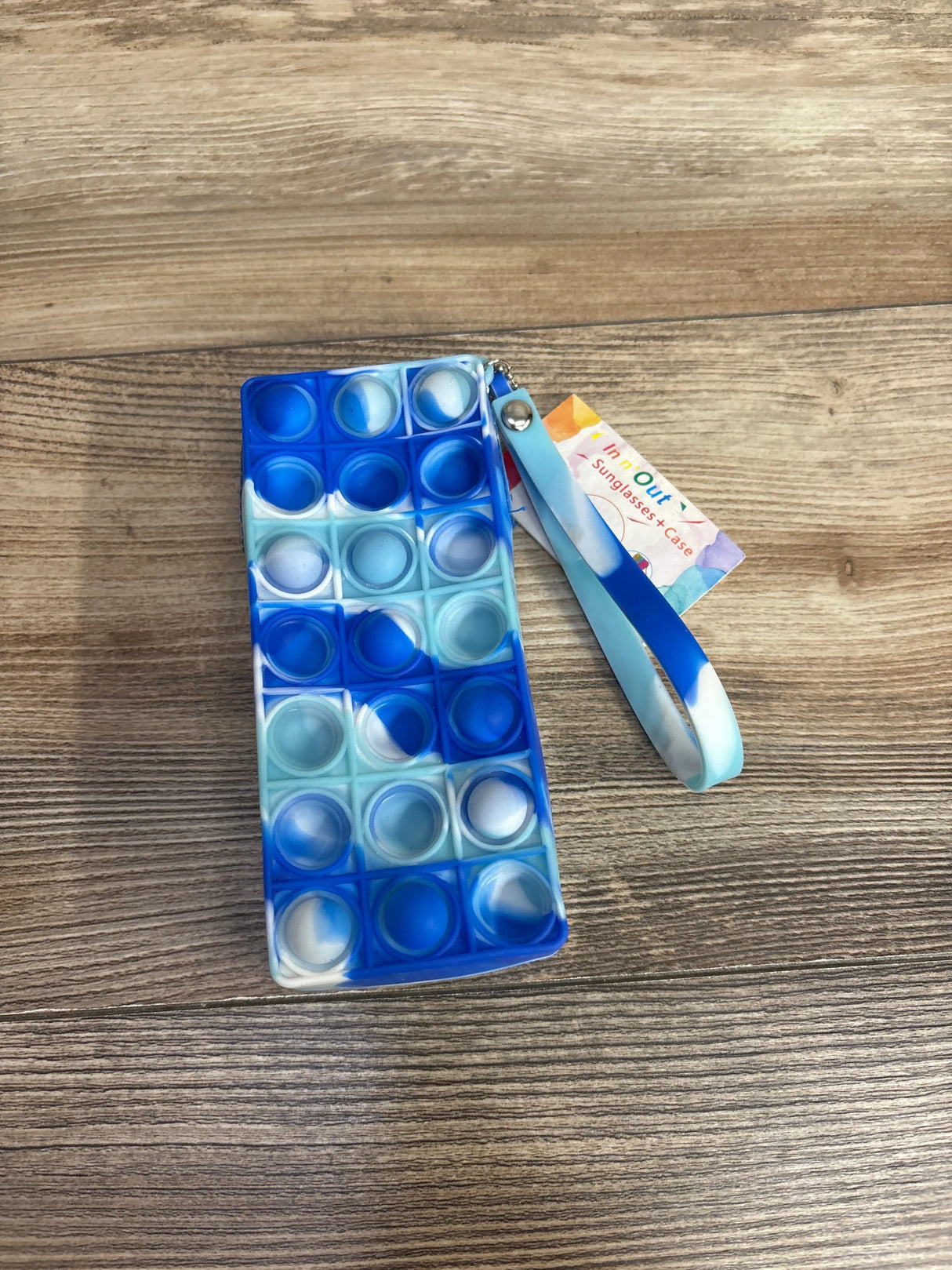 Blue and white silicone pop-it fidget toy sunglasses case with wrist strap on wooden surface