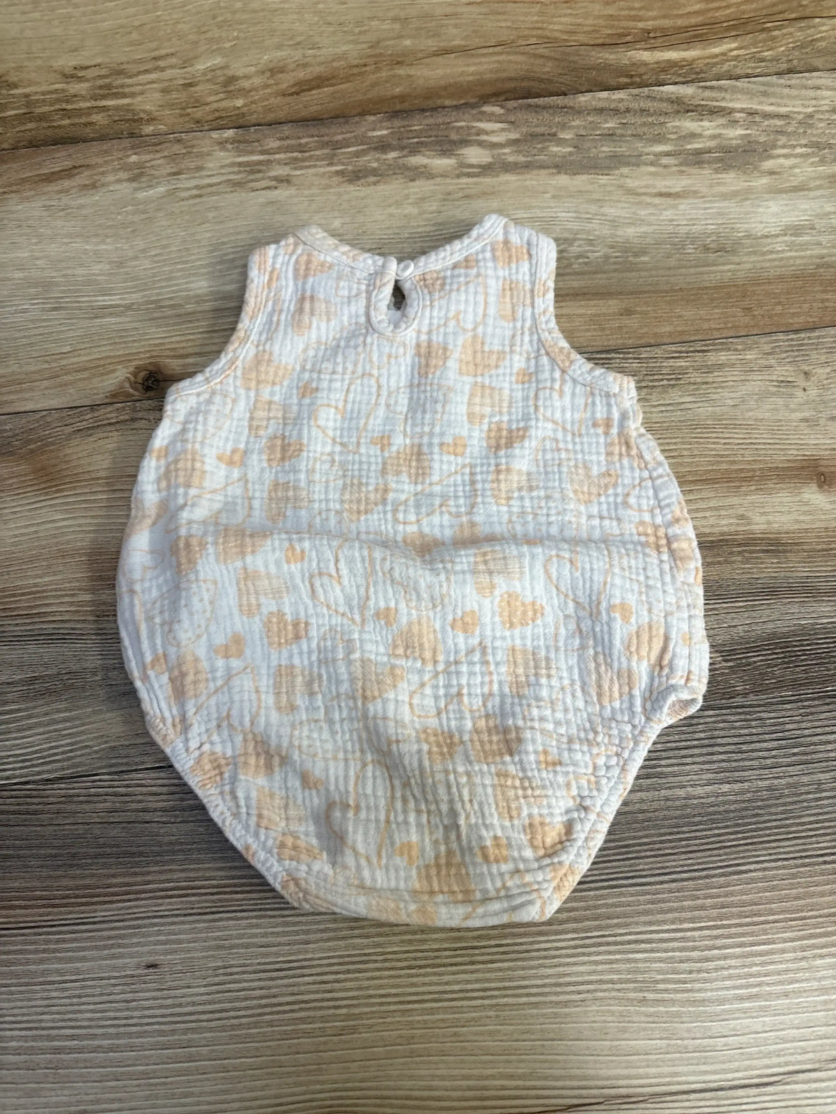 Flat lay of Chick Pea gauze bubble romper, white with peach hearts, sleeveless with back keyhole button, textured muslin on wood