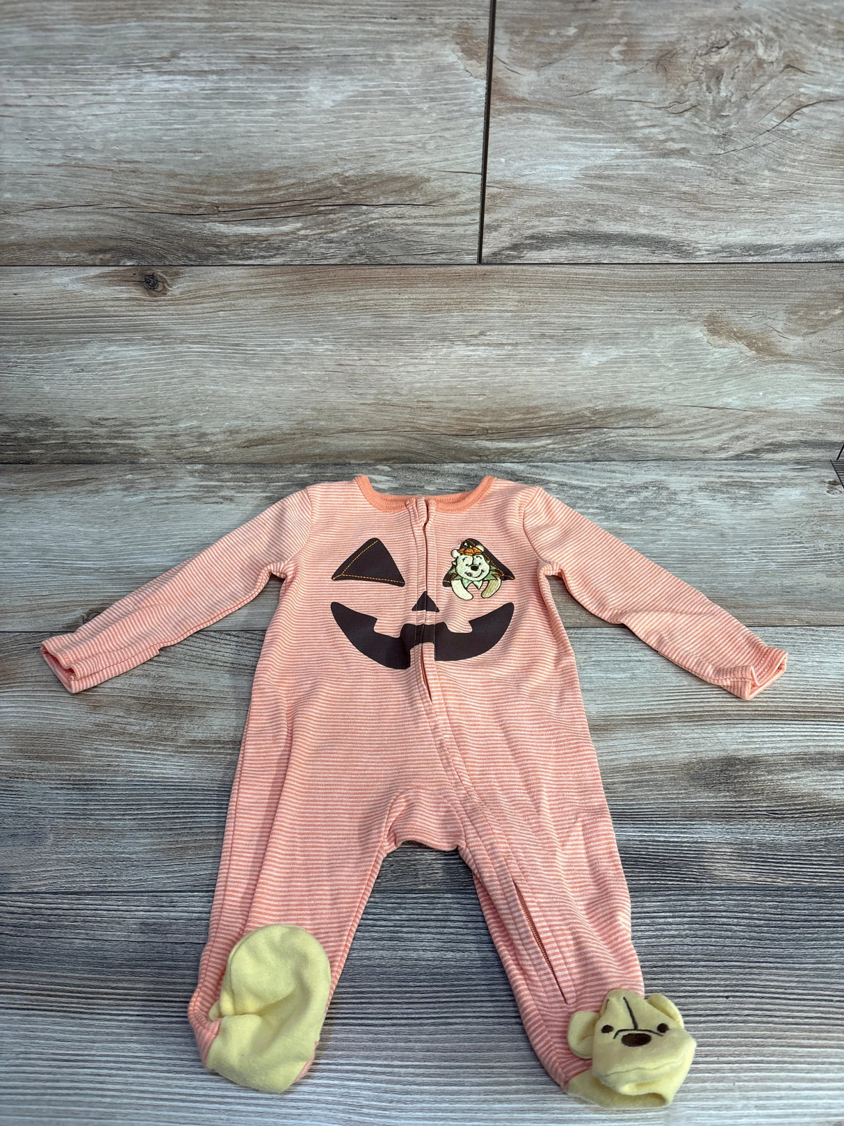 Pink striped baby onesie with pumpkin face and Winnie the Pooh feet, perfect for Halloween.