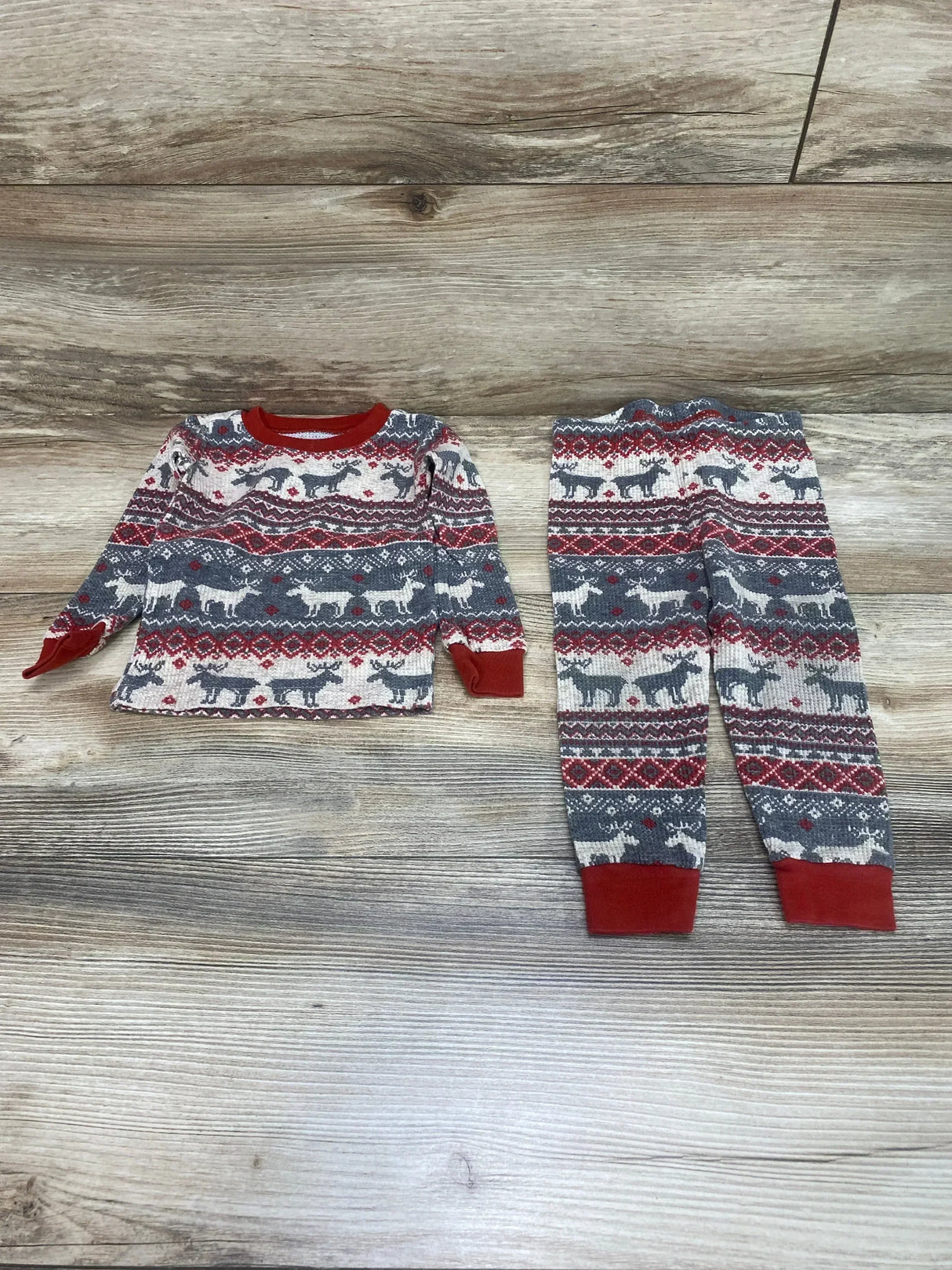 Flat lay of Children's Place 2-piece Fair Isle pajama set (9-12M) showcasing red collar and cuffs and reindeer pattern on light wood background