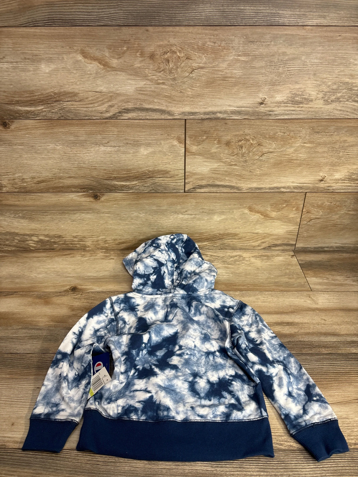 Blue and white tie-dye kids hoodie with tags, displayed on wood background.