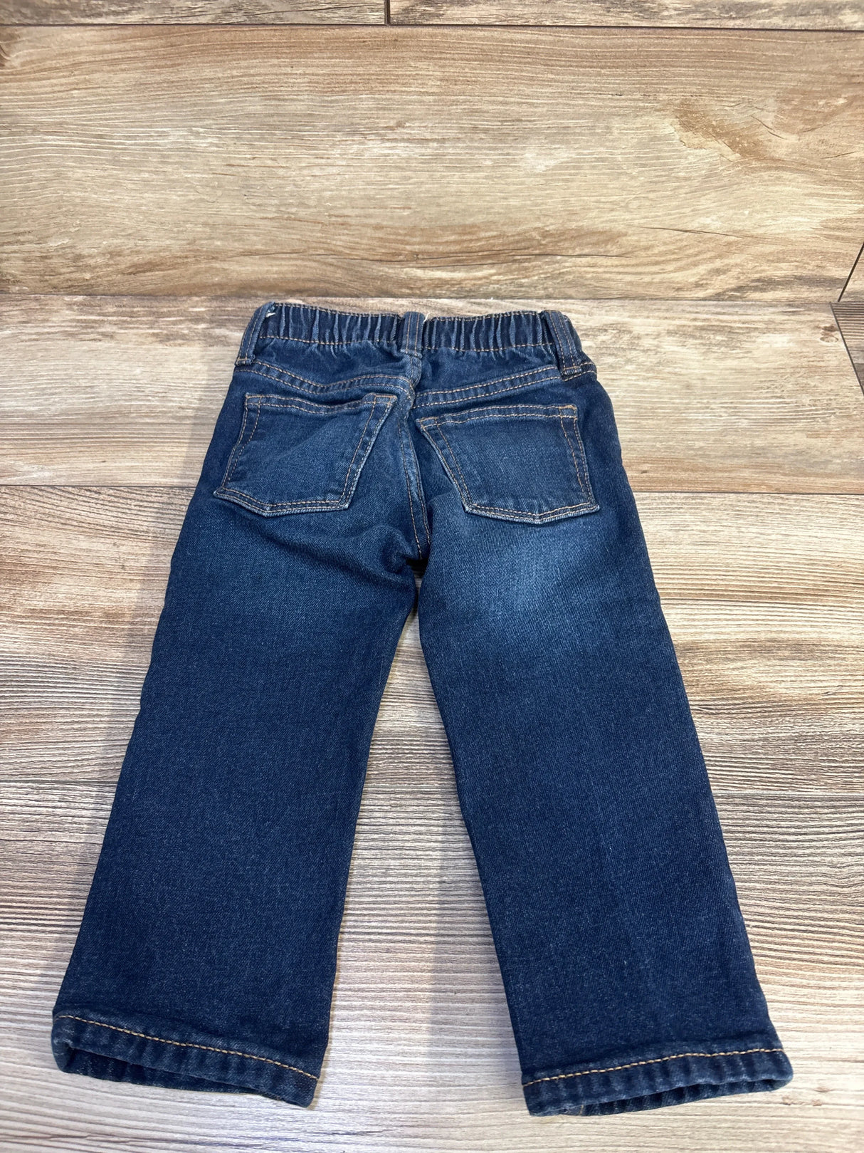 Back view of toddler blue Old Navy straight jeans showing elastic waistband and back patch pockets on wood background