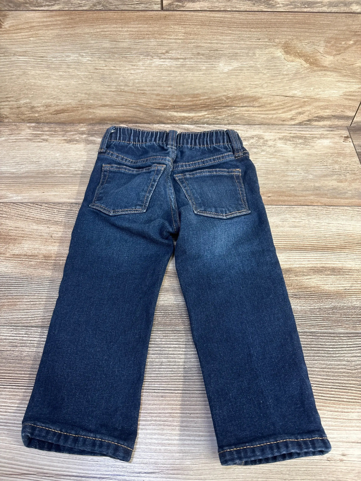 Back view of Old Navy straight leg jeans in dark blue wash denim with back patch pockets and elastic waistband on wood plank floor